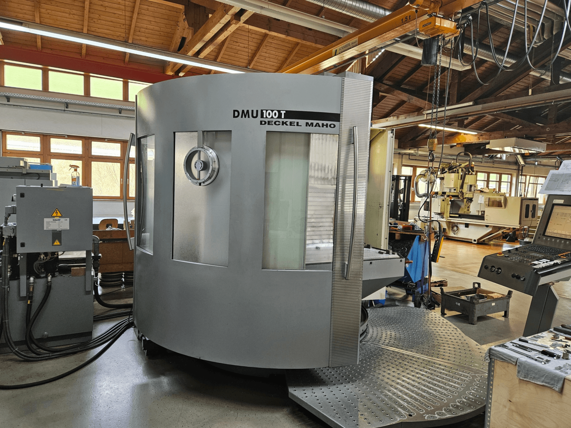 Máquina CNC DMU 100 T Deckel Maho vista de frente, con una gran base circular, panel de control y carcasa de cristal.
