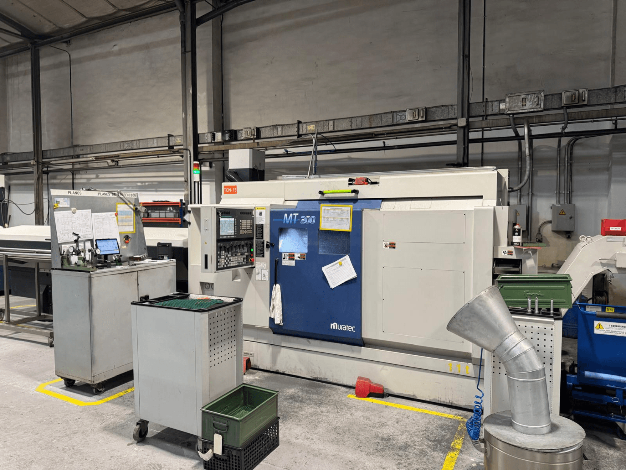 Máquina de torneado multihusillo Muratec MT200 en un entorno de fábrica, vista de frente, con panel de control y equipos circundantes.