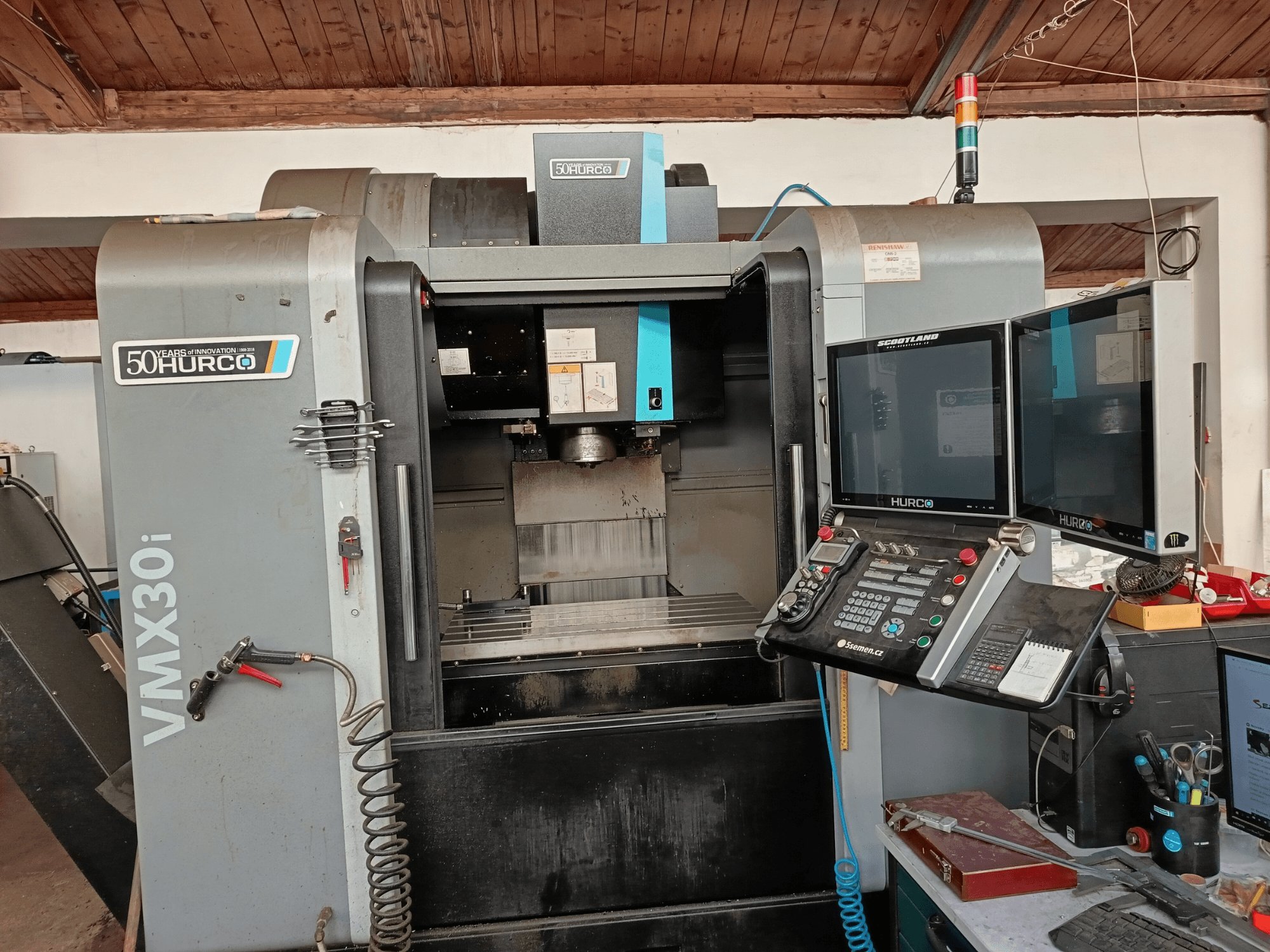 Fresadora CNC Hurco VMX30i en vista frontal, con monitores dobles, panel de control y una manguera conectada.