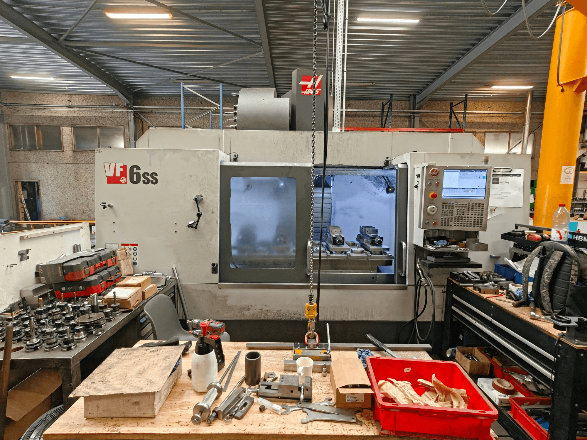 Centro de mecanizado vertical Haas VF-6SS en un taller; vista lateral en la que se aprecian el panel de control y el desorden del espacio de trabajo, repleto de herramientas.