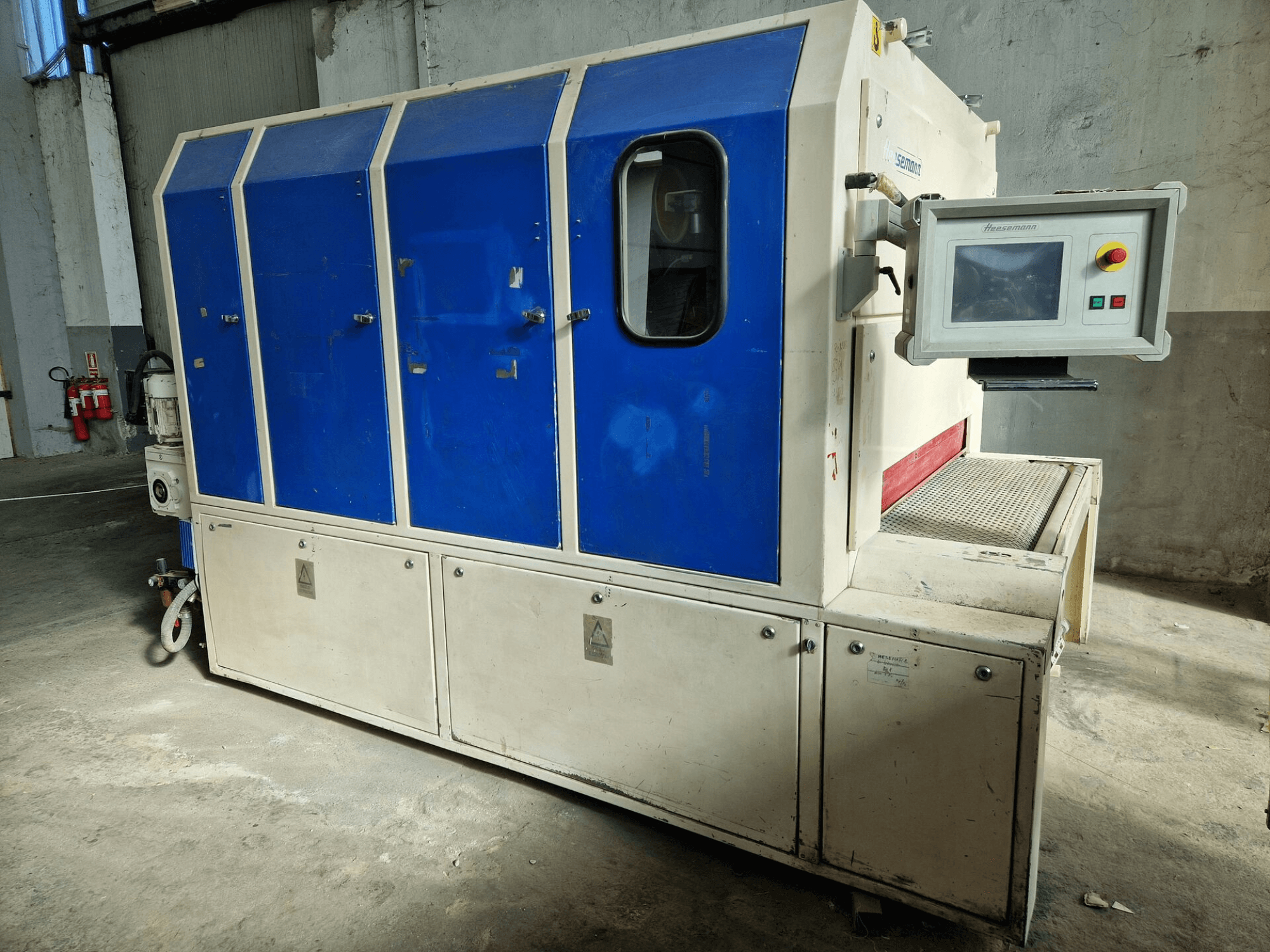 Máquina industrial de la marca "Sedecom", vista lateral; presenta paneles azules, una pantalla de control y una superficie texturizada para manipular productos.