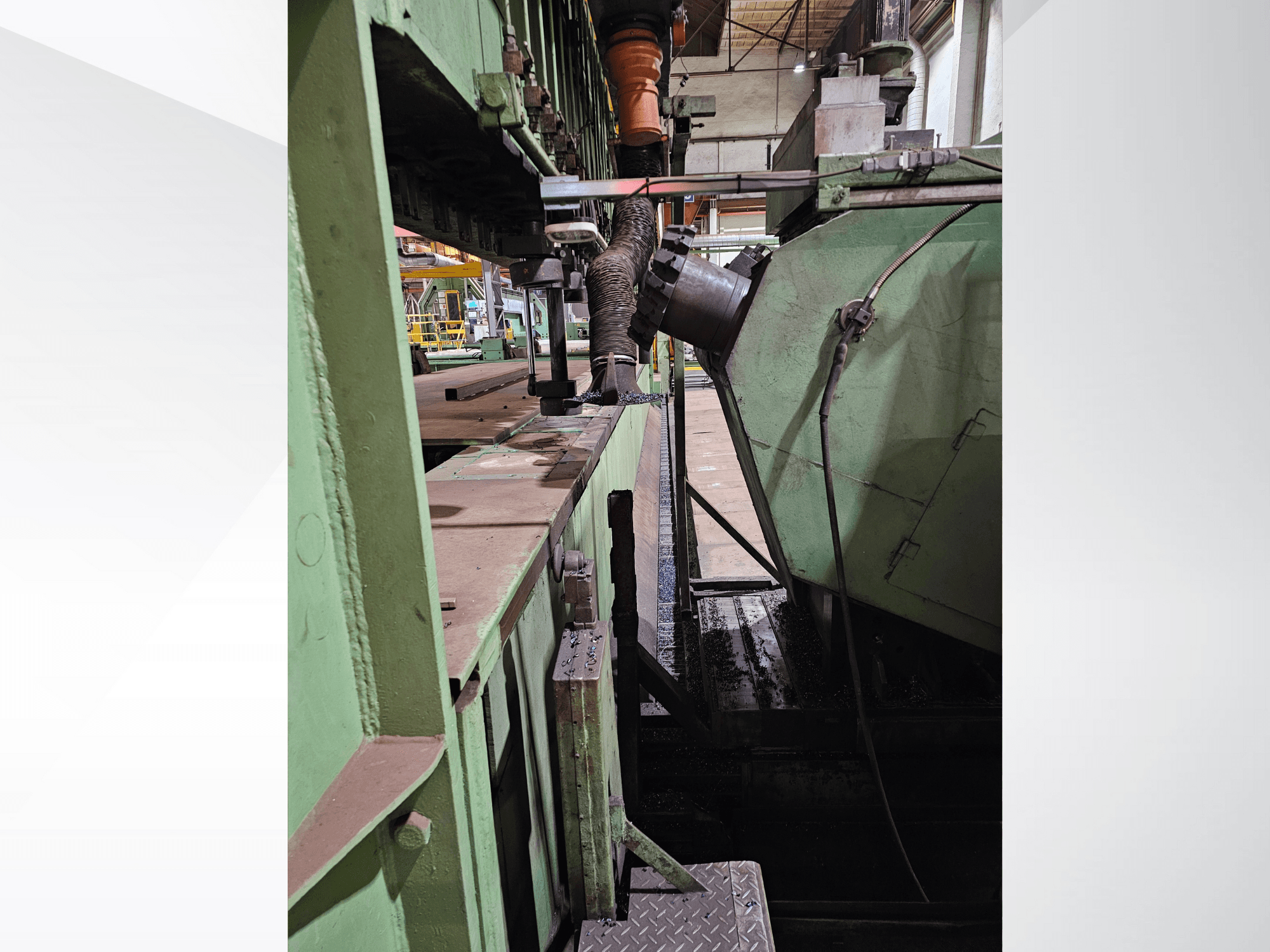 Maquinaria industrial verde con una vista lateral de una tolva y un mecanismo de alimentación, mostrando componentes metálicos y una plataforma.