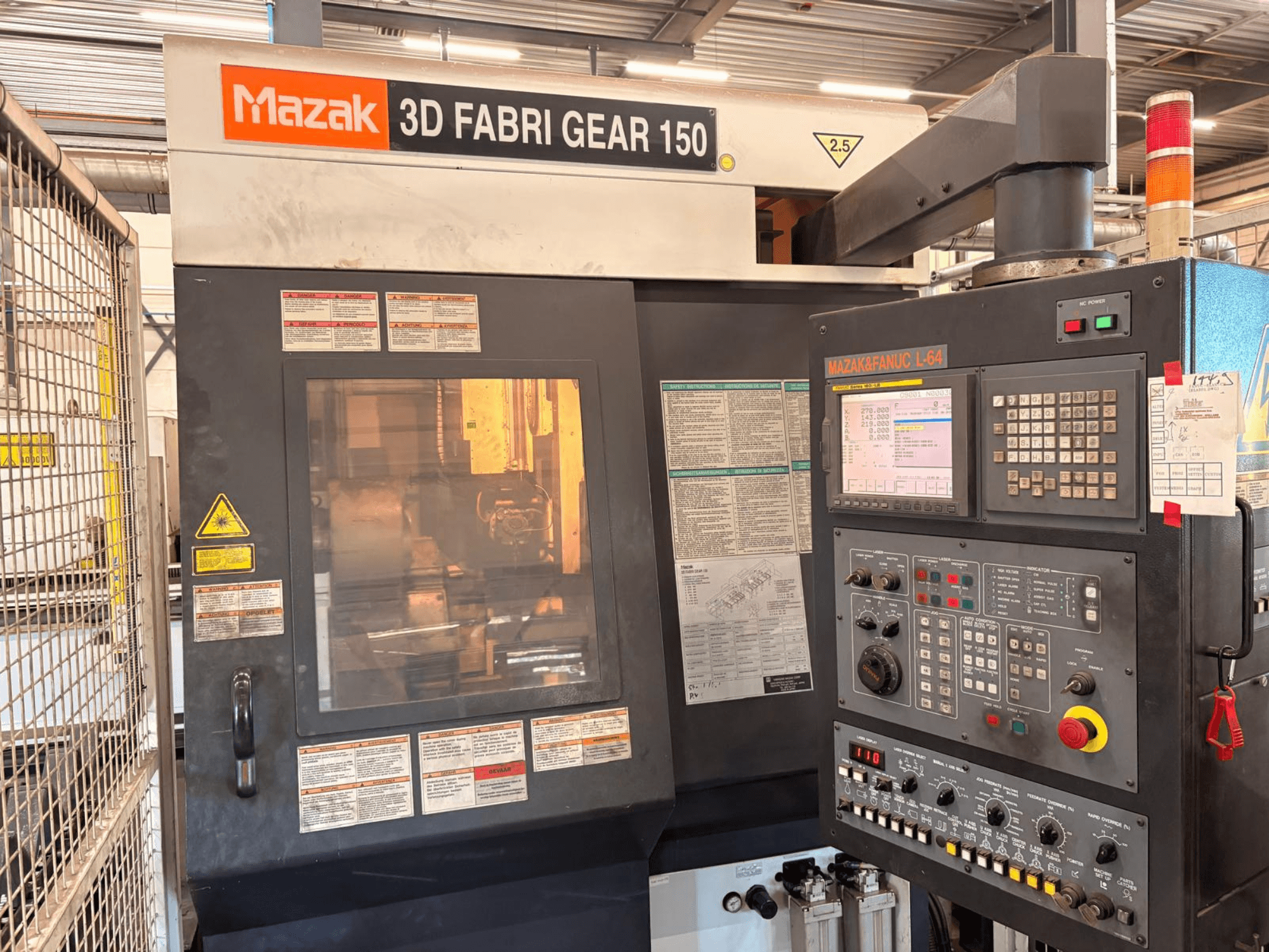 Máquina de corte de tubos Mazak 3D Fabri Gear 150; vista frontal en la que se aprecian el panel de control, las etiquetas de seguridad y la interfaz de funcionamiento.
