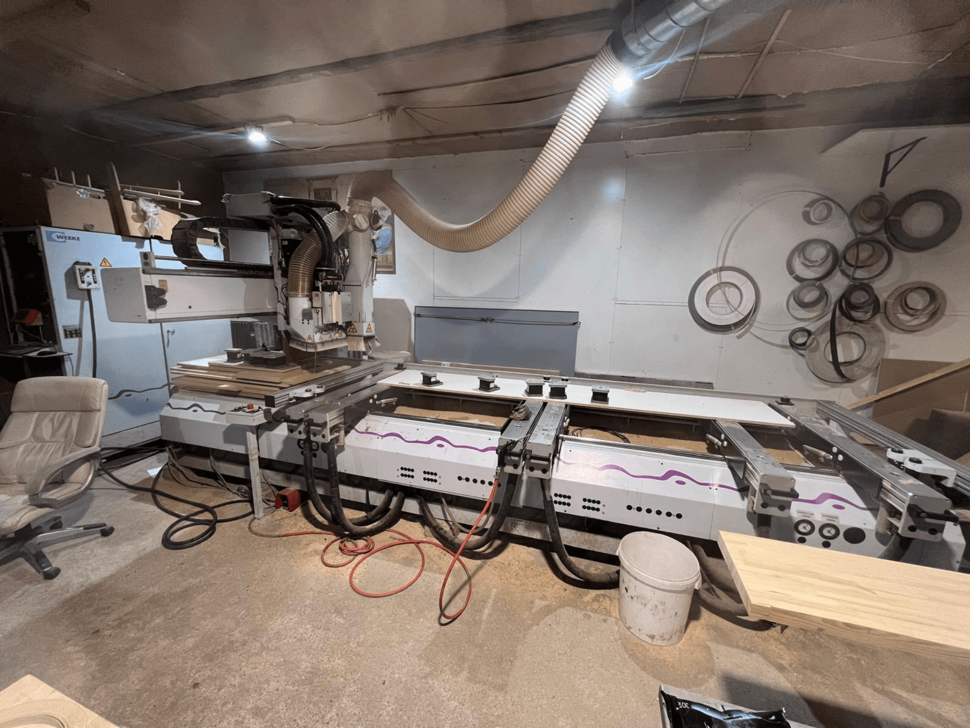 Centro de mecanizado de madera CNC Weeke OPTIMAT BP 120 en el taller, vista frontal con piezas de madera y herramientas visibles sobre la superficie.