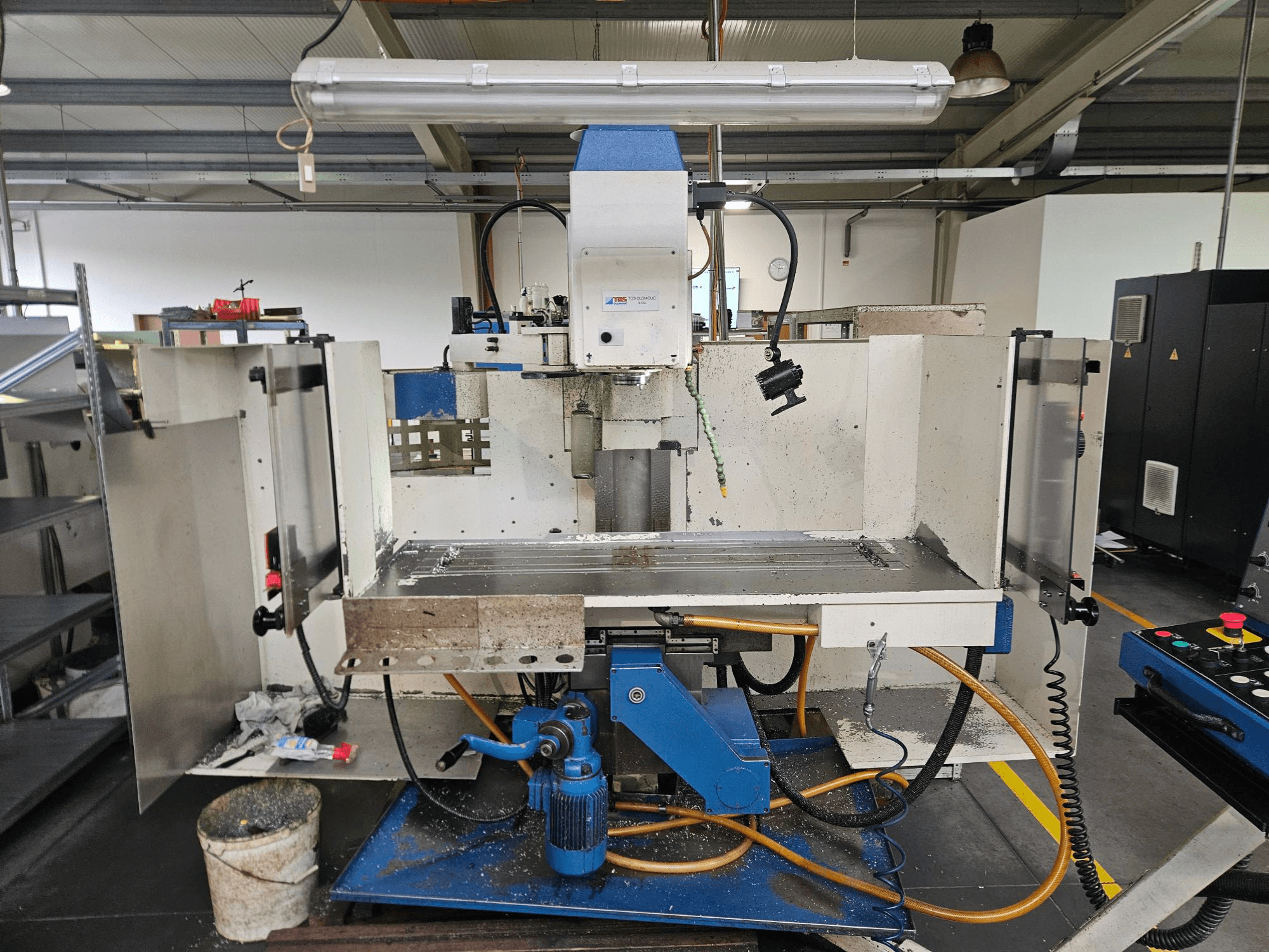 CNC TOS Olomouc FV30 Un centro de mecanizado vertical en un taller, vista frontal que muestra el panel de control, la mesa de trabajo y el sistema de refrigeración.