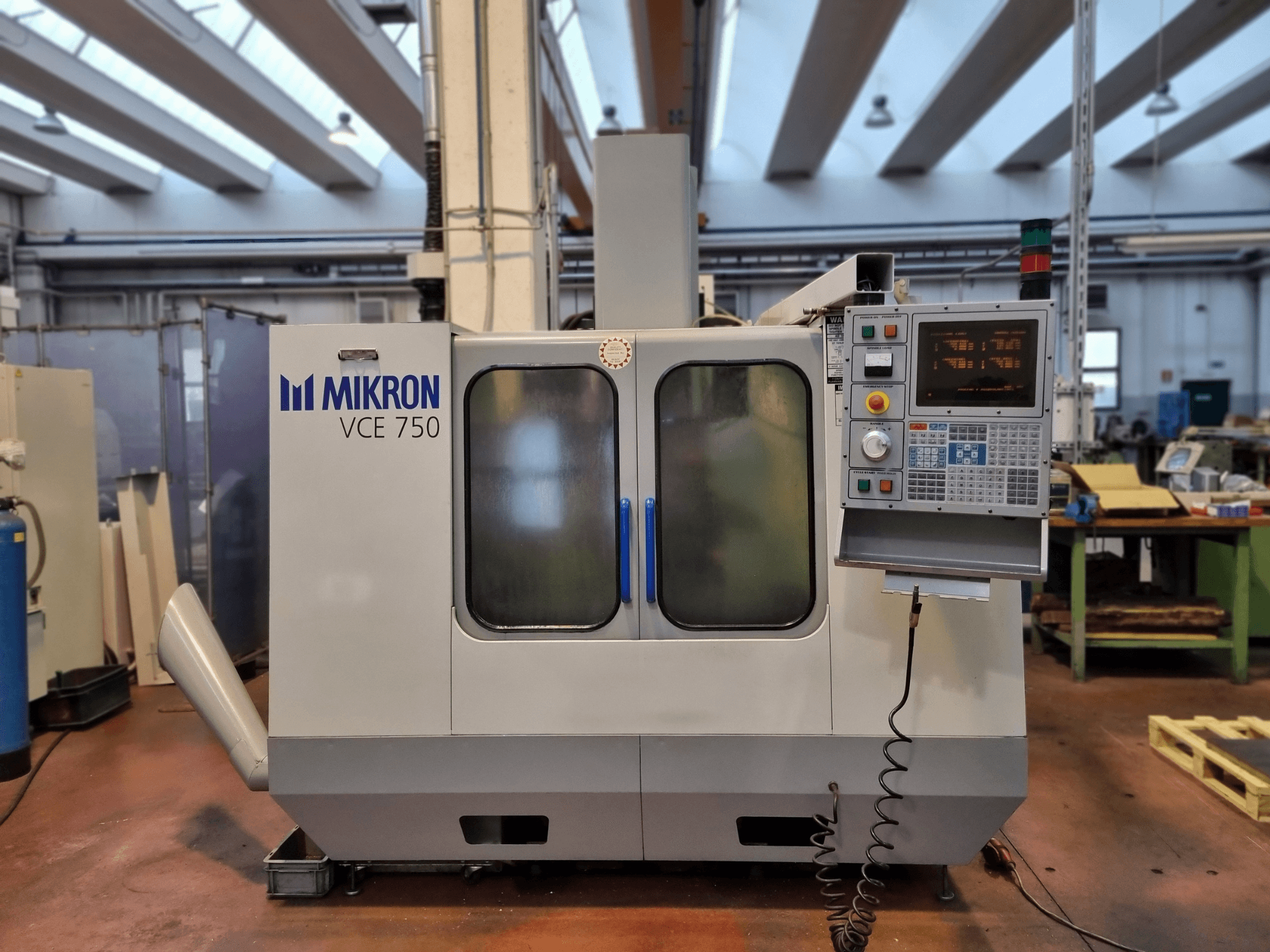 Máquina CNC Mikron VCE 750 blanca en un taller, vista lateral, con panel de control digital y grandes puertas de cristal.