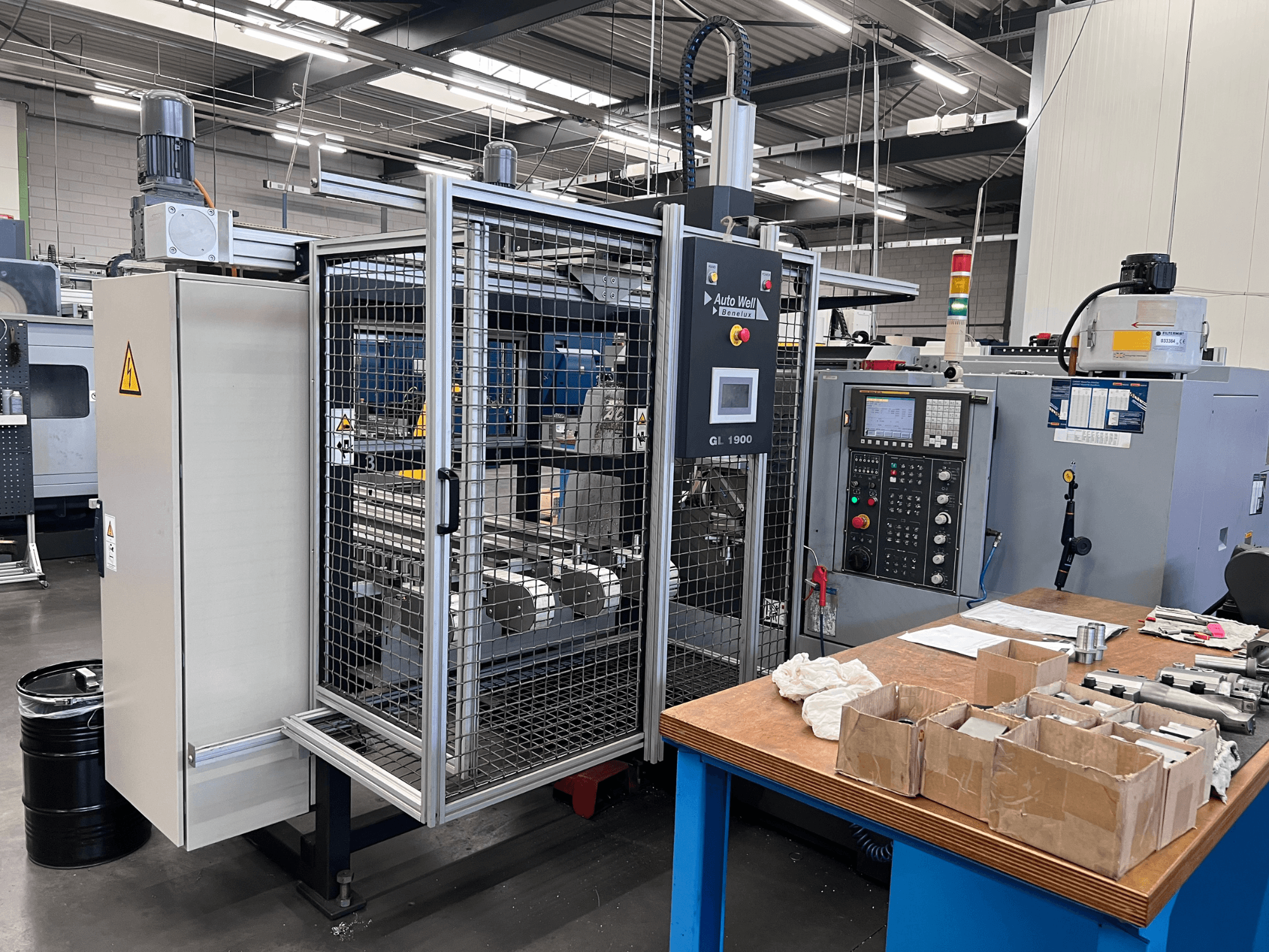 Vista frontal de la máquina Auto Weld GL 1900 con panel de control, caja de seguridad y herramientas circundantes en un banco de trabajo.