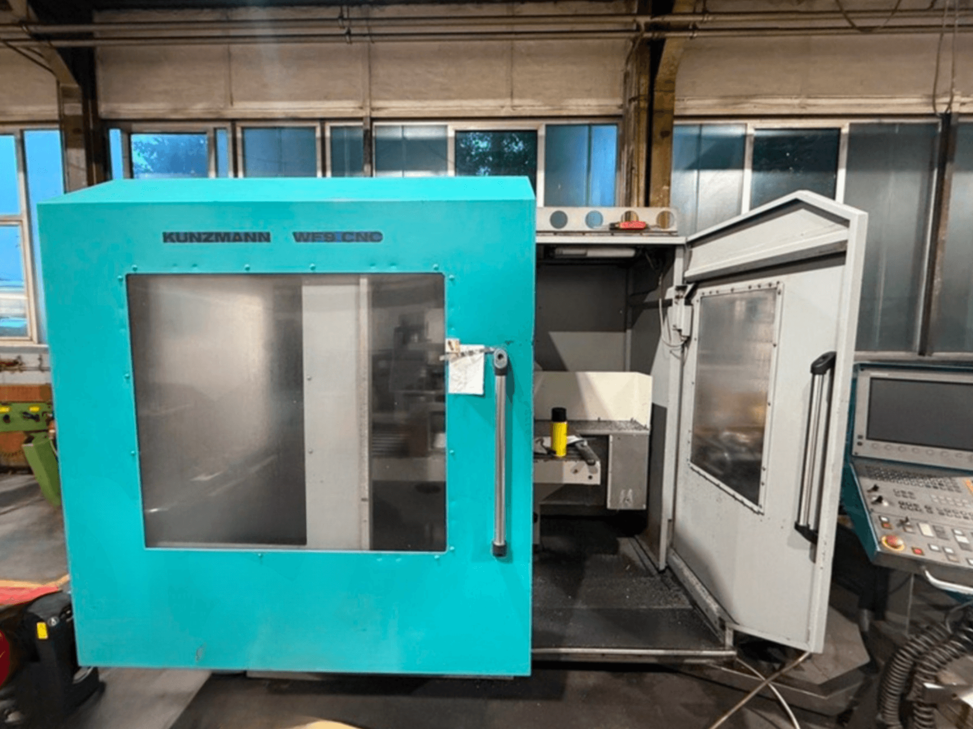 Centro de mecanizado vertical CNC KUNZMANN WF9, vista frontal con las puertas abiertas, mostrando el interior y el panel de control.
