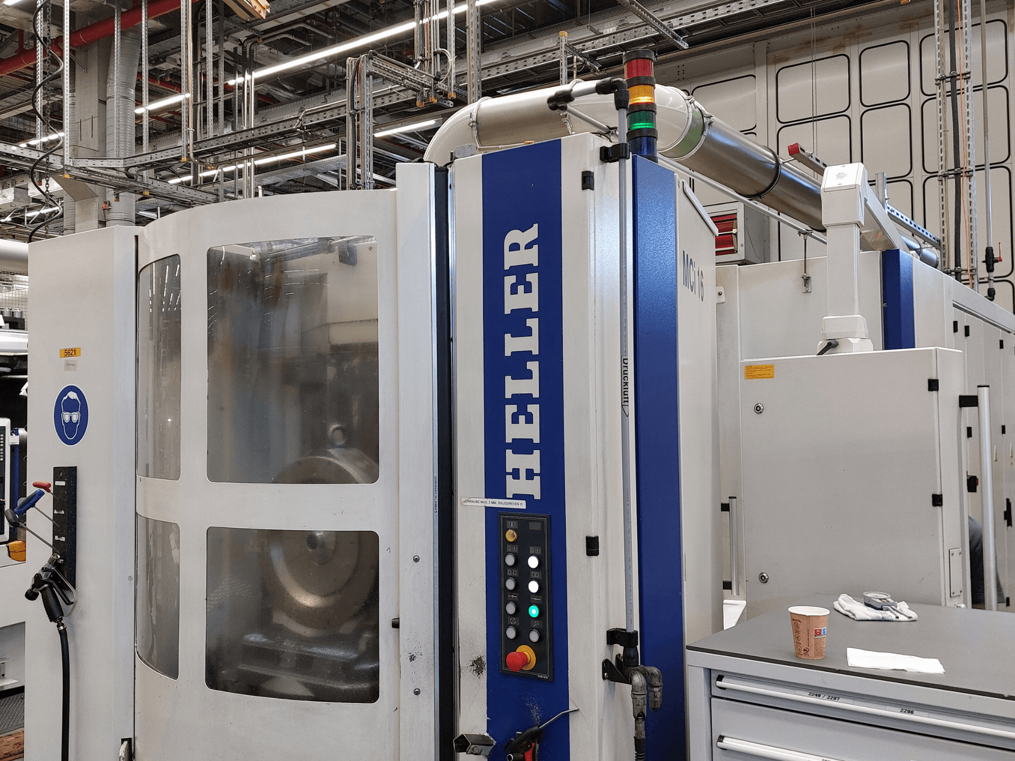 Centro de mecanizado vertical Heller MCI 16 en un entorno industrial, con panel de control y señalización de seguridad.