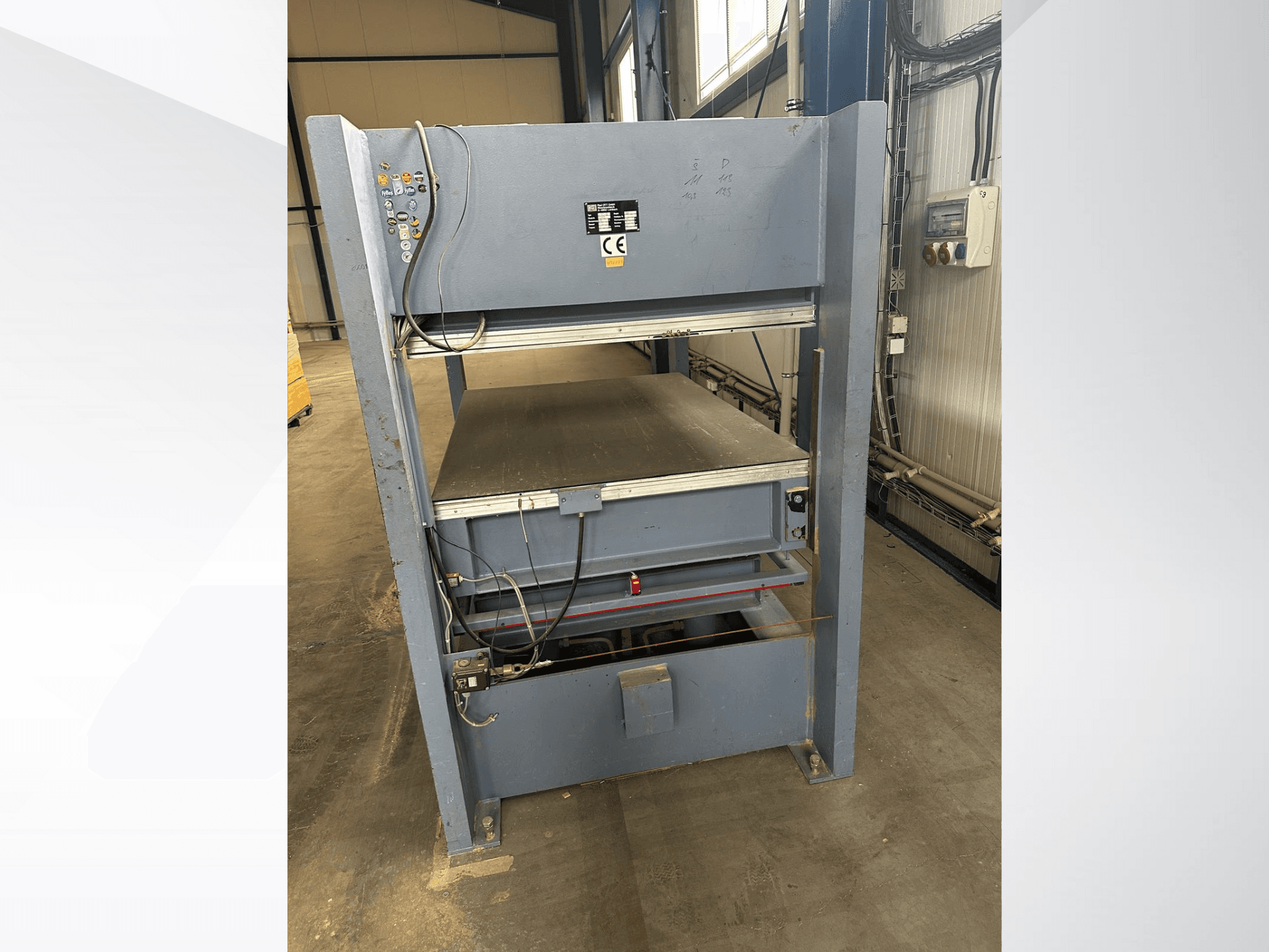 Máquina industrial gris con panel de control, vista de frente; incluye plataformas ajustables y marcas de seguridad.