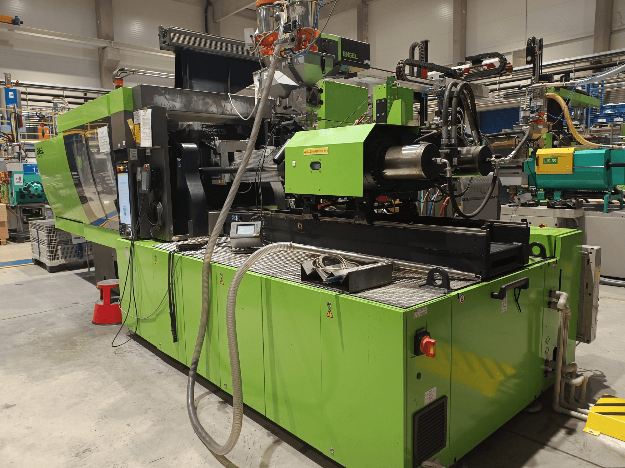 Máquina de moldeo por inyección Engel, vista lateral, exterior verde, con panel de pantalla táctil y componentes hidráulicos visibles.
