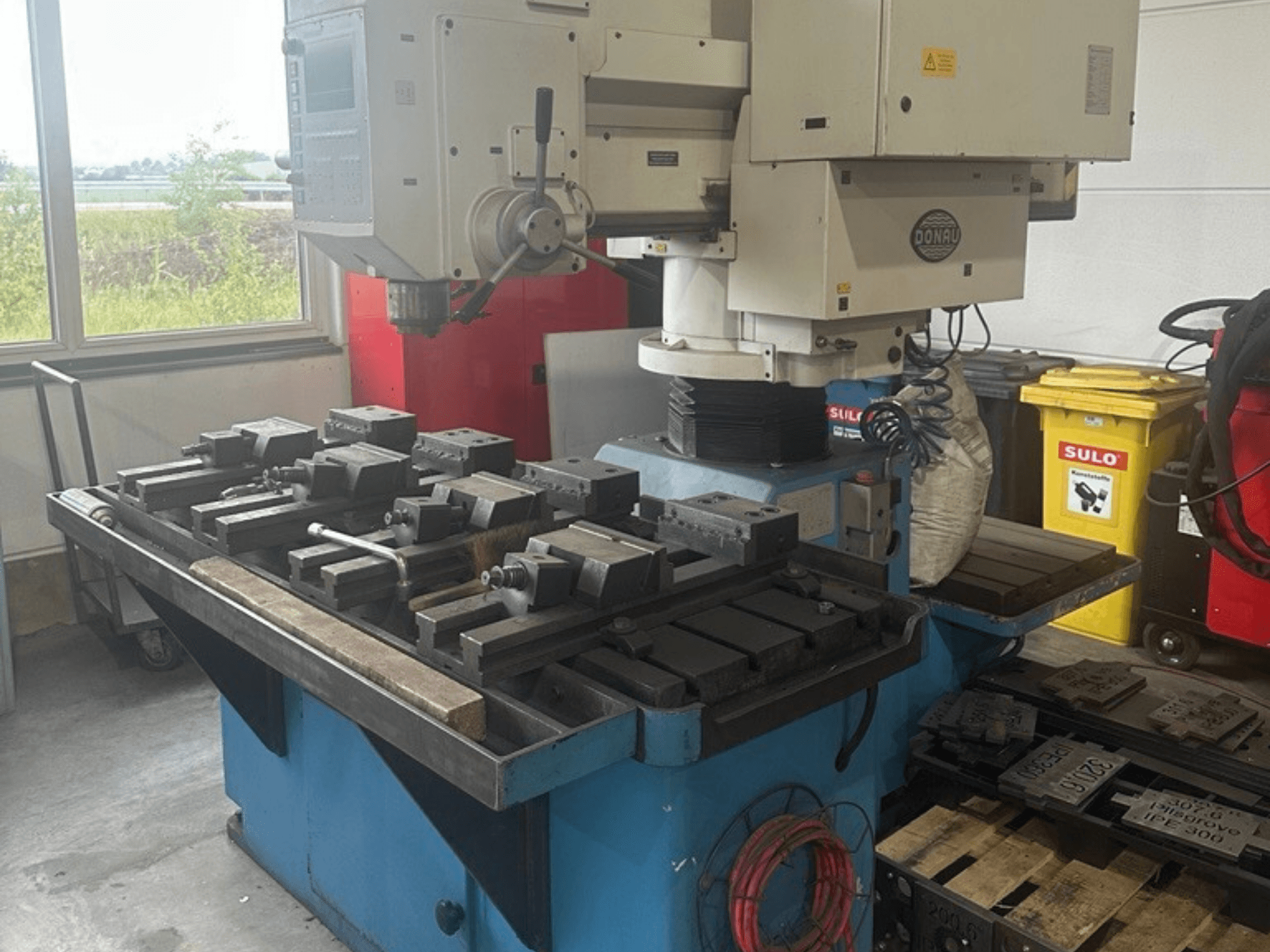 Centro de mecanizado vertical DONAU Danumeric 440 en un taller, equipado con una mesa portaherramientas y diversos componentes acoplados.