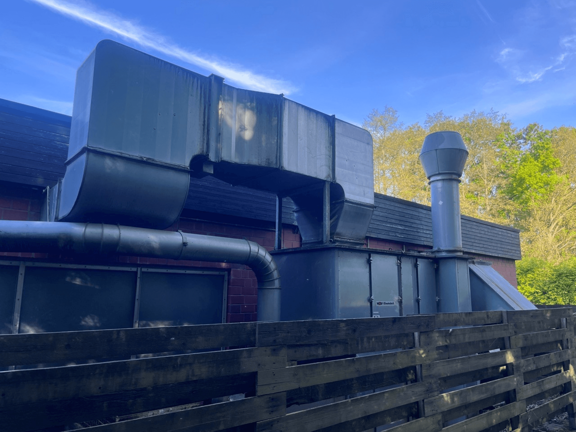 Sistema de ventilación industrial con conductos metálicos, vista lateral; incluye una chimenea cuadrada y otra cilíndrica, acabado verde.