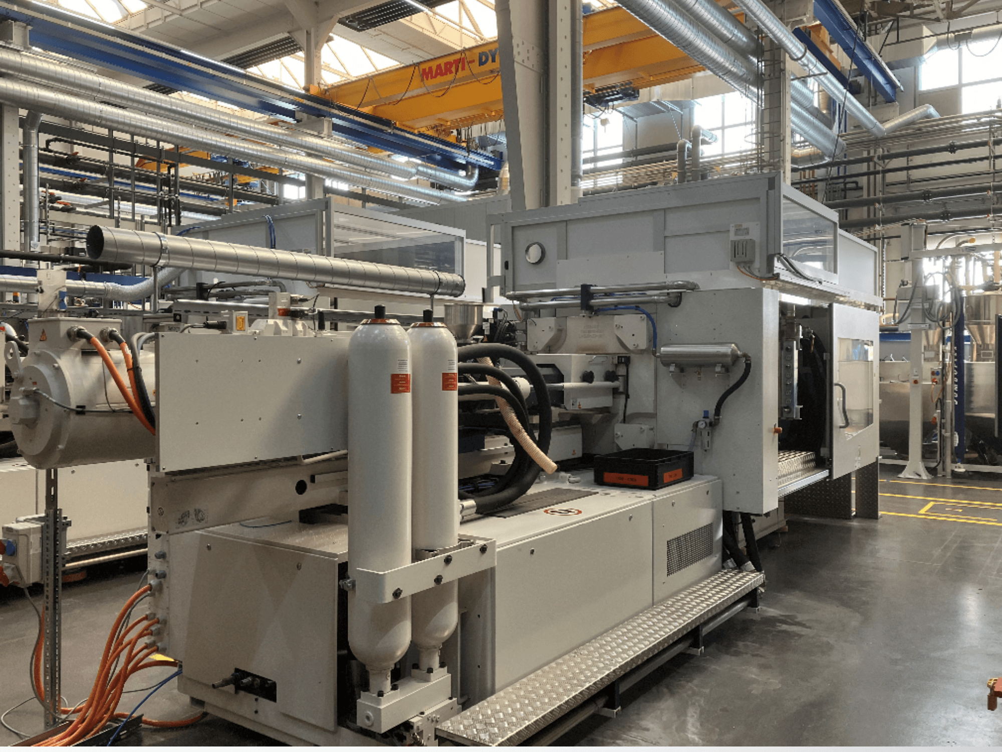 Máquina industrial mostrada en vista lateral con múltiples mangueras, dos depósitos verticales y panel de control; marca/modelo no visible.