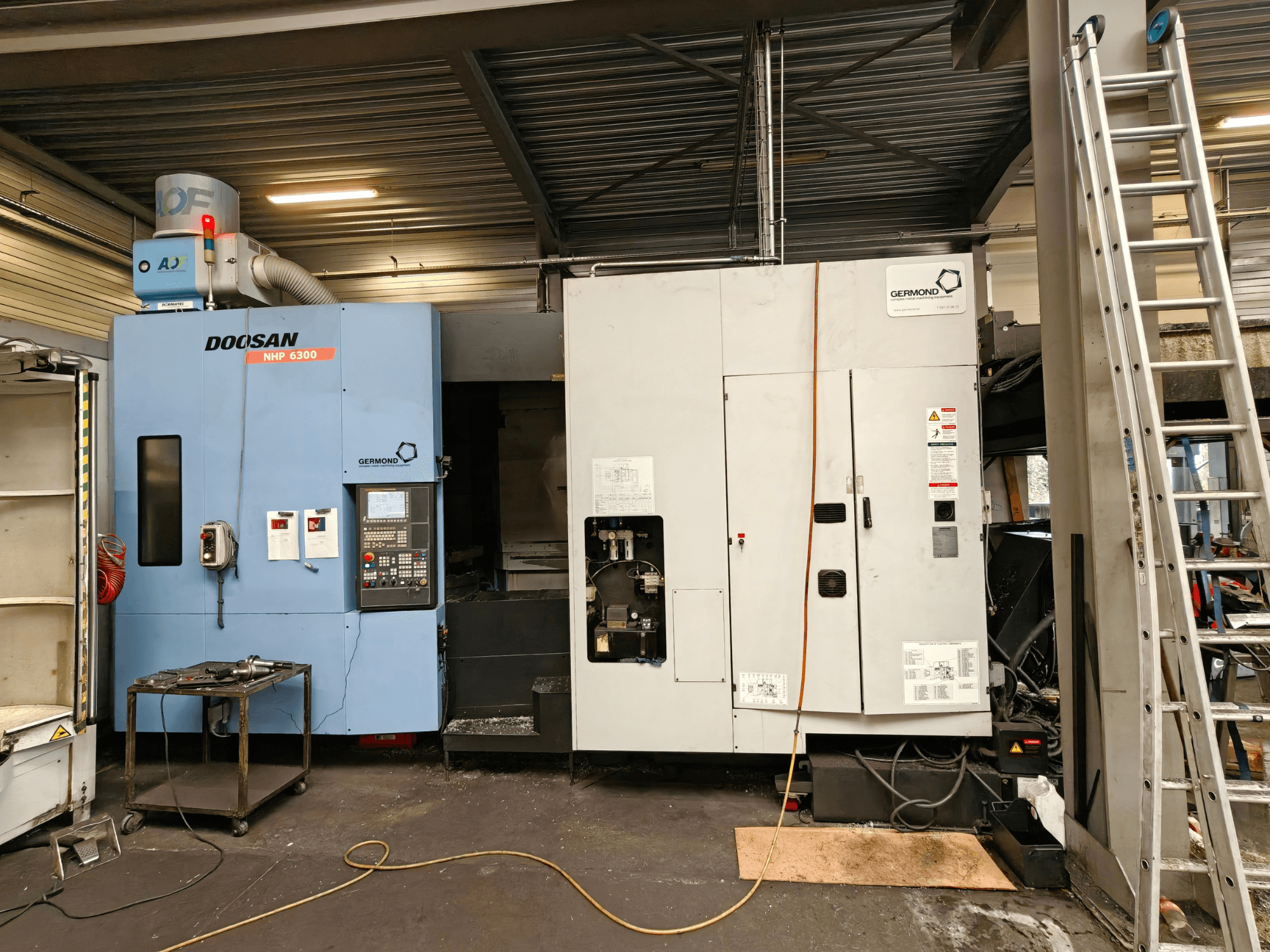 Centro de mecanizado horizontal DOOSAN NHP6300 visto de frente, en el que se aprecian el panel de control y la maquinaria adyacente en un entorno de taller.