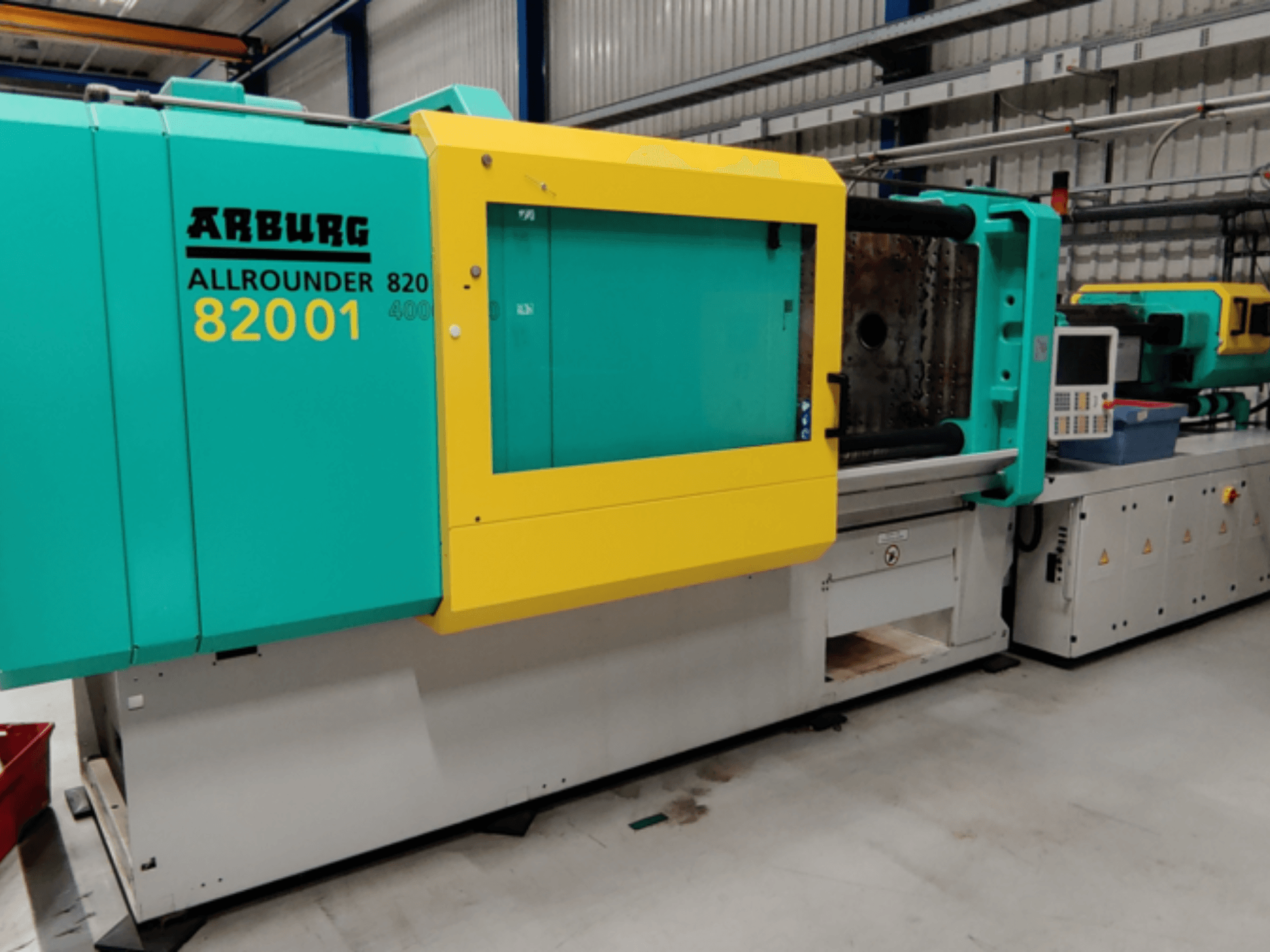 Máquina de moldeo por inyección Arburg ALLROUNDER 82001 en verde azulado y amarillo, vista lateral que muestra el panel de control y las características operativas.