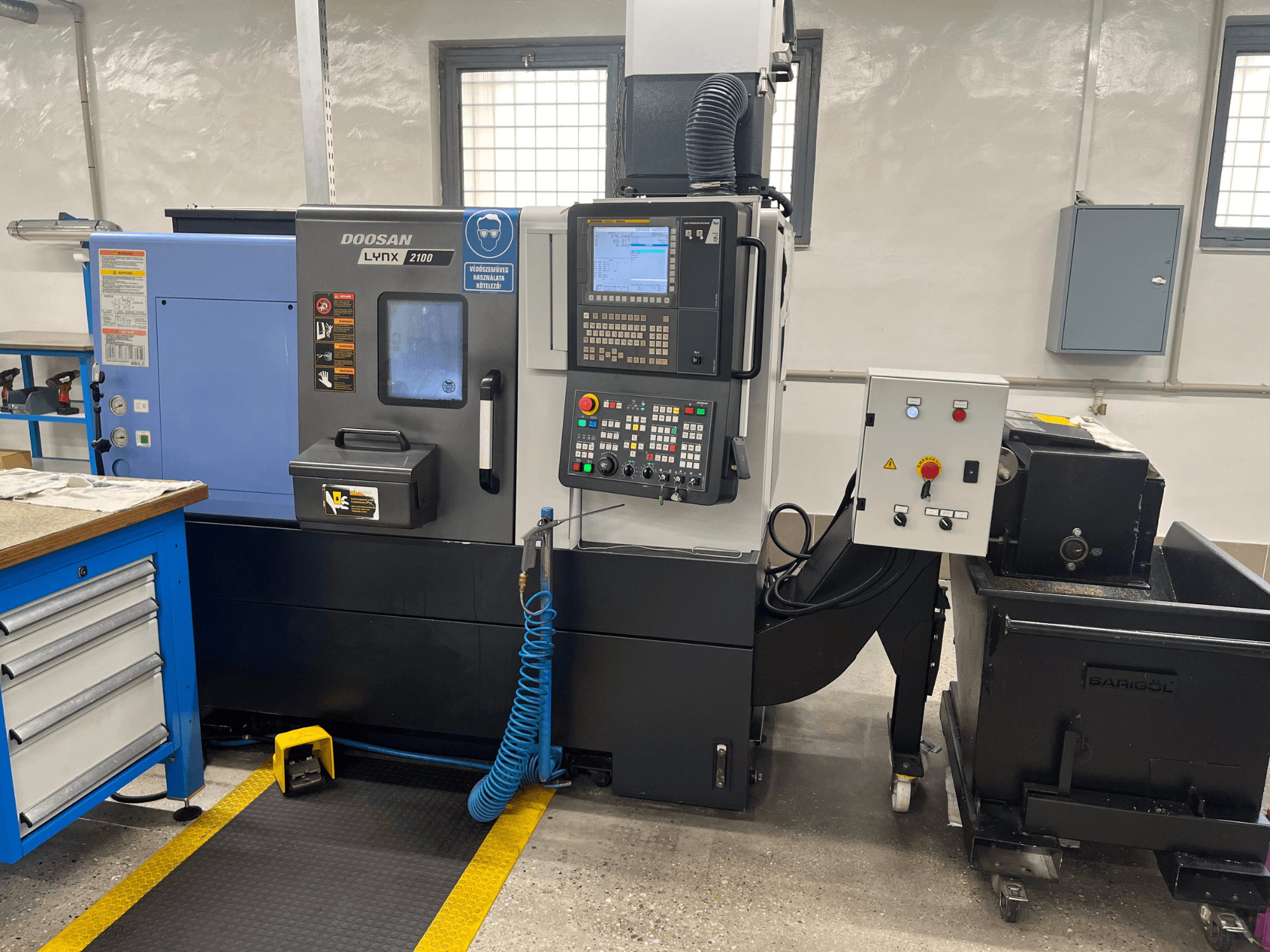 Torno Doosan Lynx 210 en taller, mostrando panel de control, almacenamiento de herramientas y sistema de refrigeración, vista lateral con detalles del espacio de trabajo.