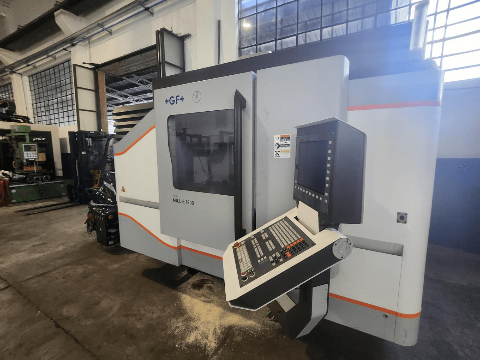 GF MILL E1200, vista frontal de fresadora con panel de control, pantalla de visualización y etiquetas de seguridad, en entorno de taller.