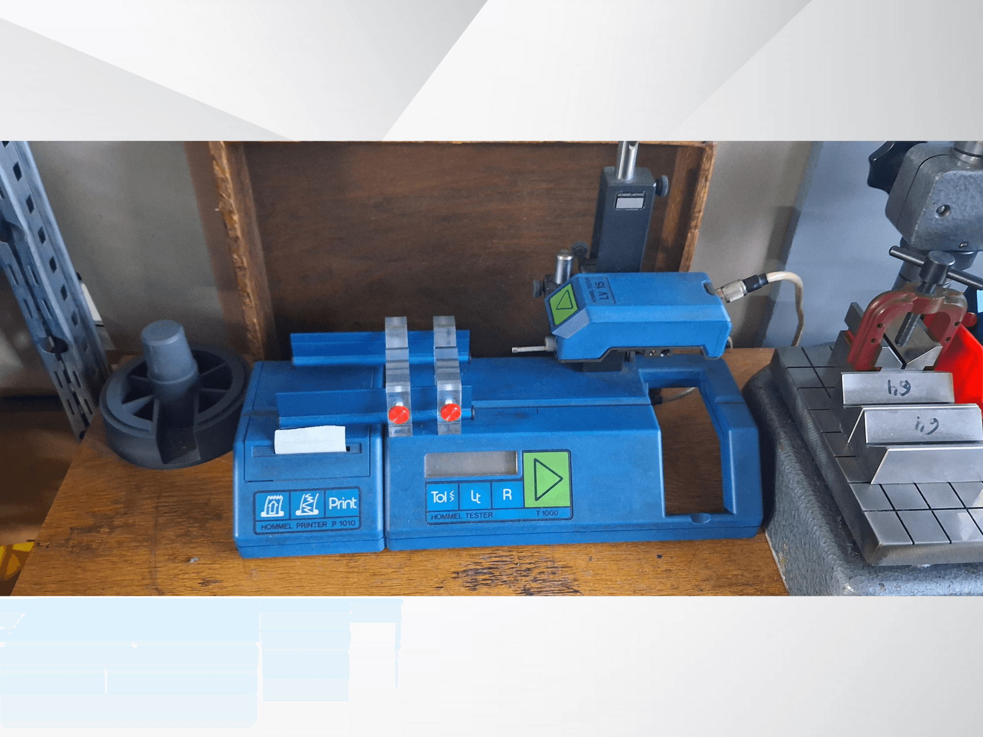 Impresora Hommel T 1000 azul y comprobador T 1 010 con botones rojos, vistos de frente sobre un banco de trabajo con bloques metálicos.