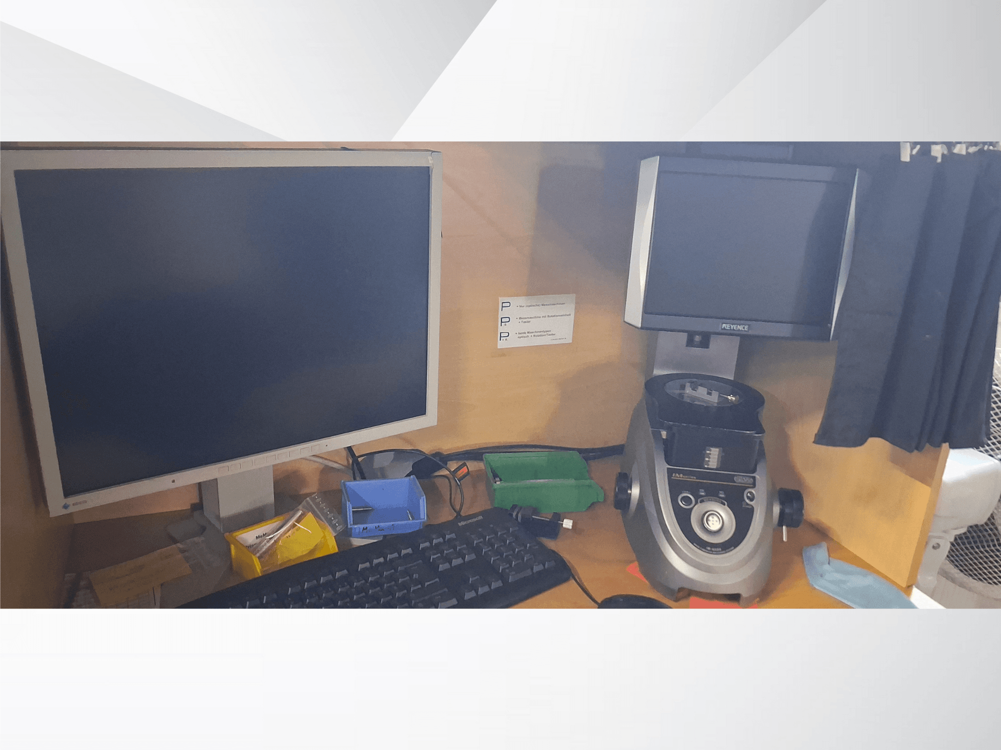 Monitor de ordenador con teclado, pantalla de marca PEVA y un aparato de laboratorio gris sobre un escritorio de madera con bandejas y papeles variados.