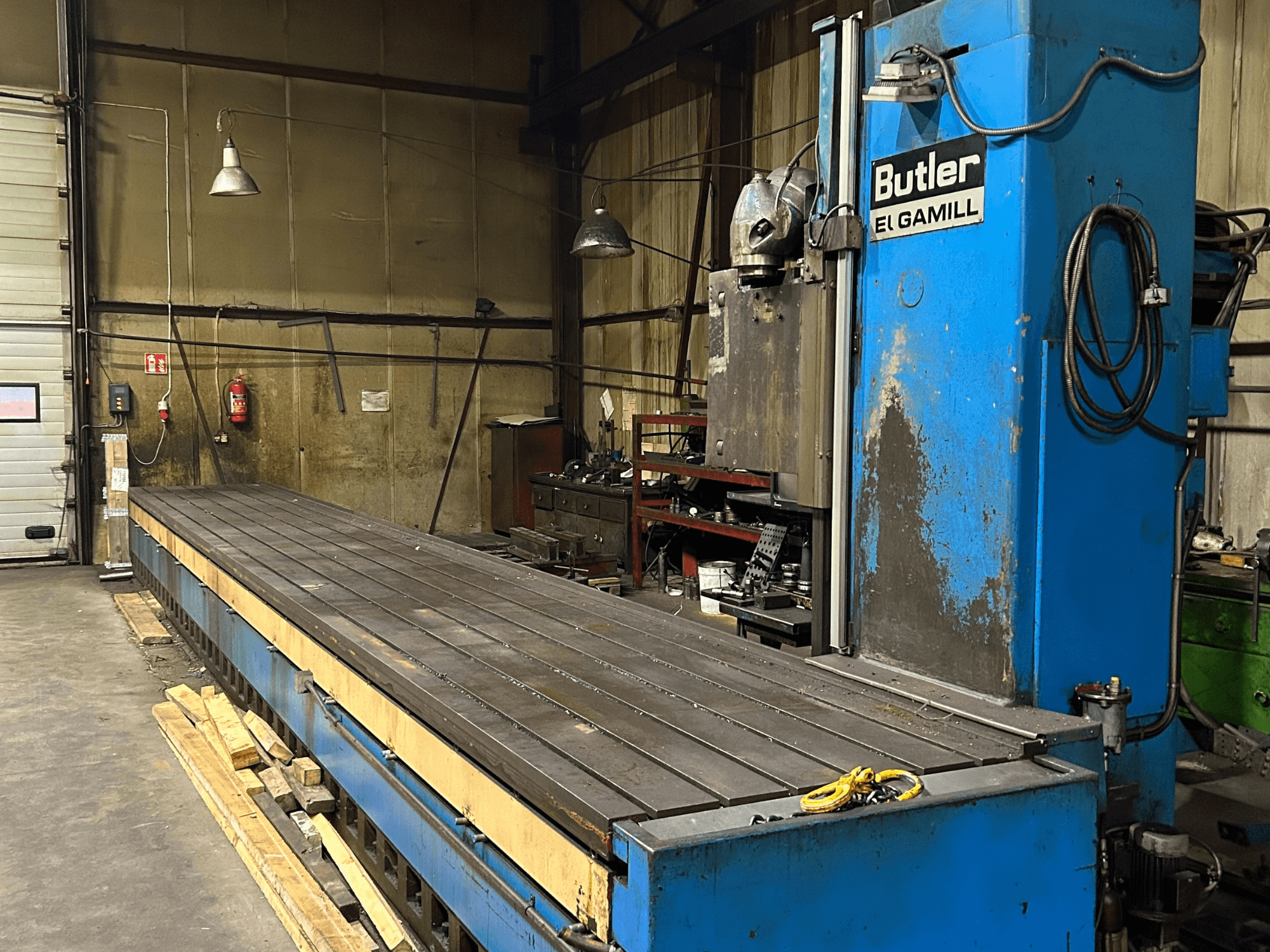 Fresadora Blue Butler El Gamill en un taller, vista lateral mostrando una larga mesa plana y los controles a la derecha.