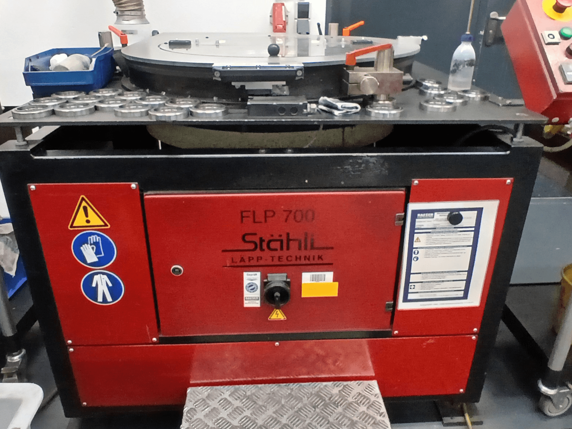 Máquina herramienta STAHLI FLP 700, vista frontal, con controles de funcionamiento, advertencias de seguridad y componentes sobre una superficie metálica.