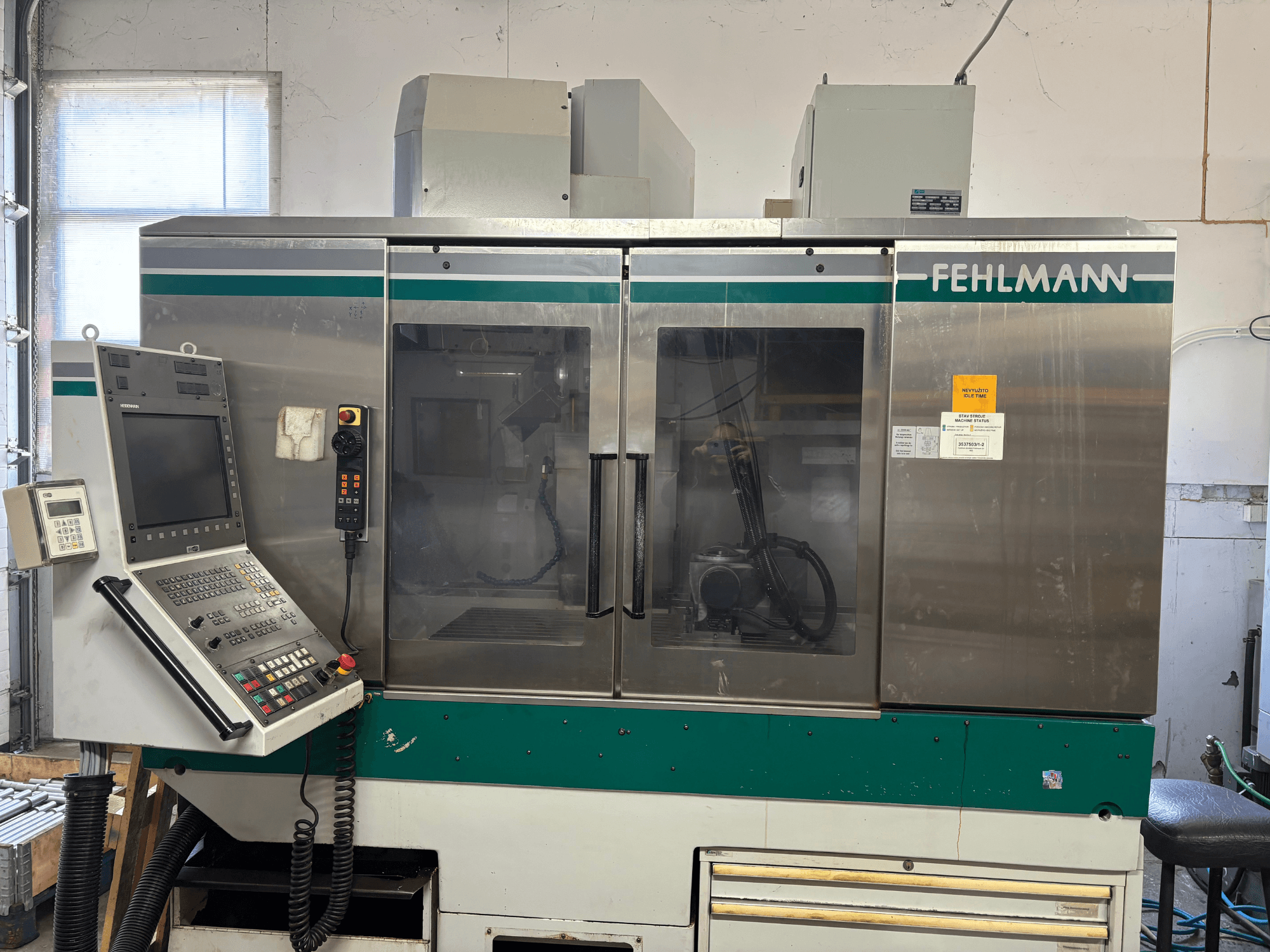 Vista frontal del centro de mecanizado vertical FEHLMANN Picomax 90-M, en la que se aprecian el panel de control, la carcasa transparente y los botones de funcionamiento.