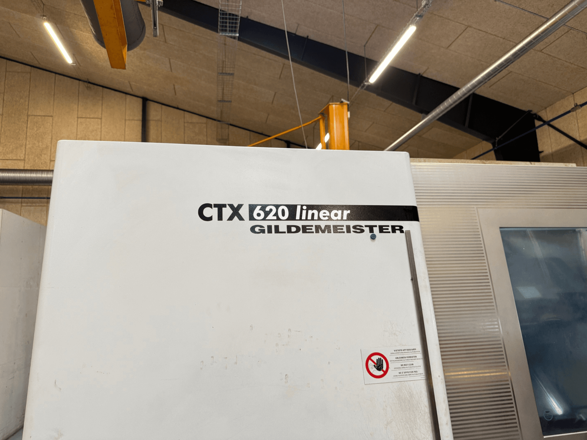 Vista lateral de la máquina CTX 620 Linear Gildemeister, con exterior blanco y etiquetas de advertencia de seguridad.