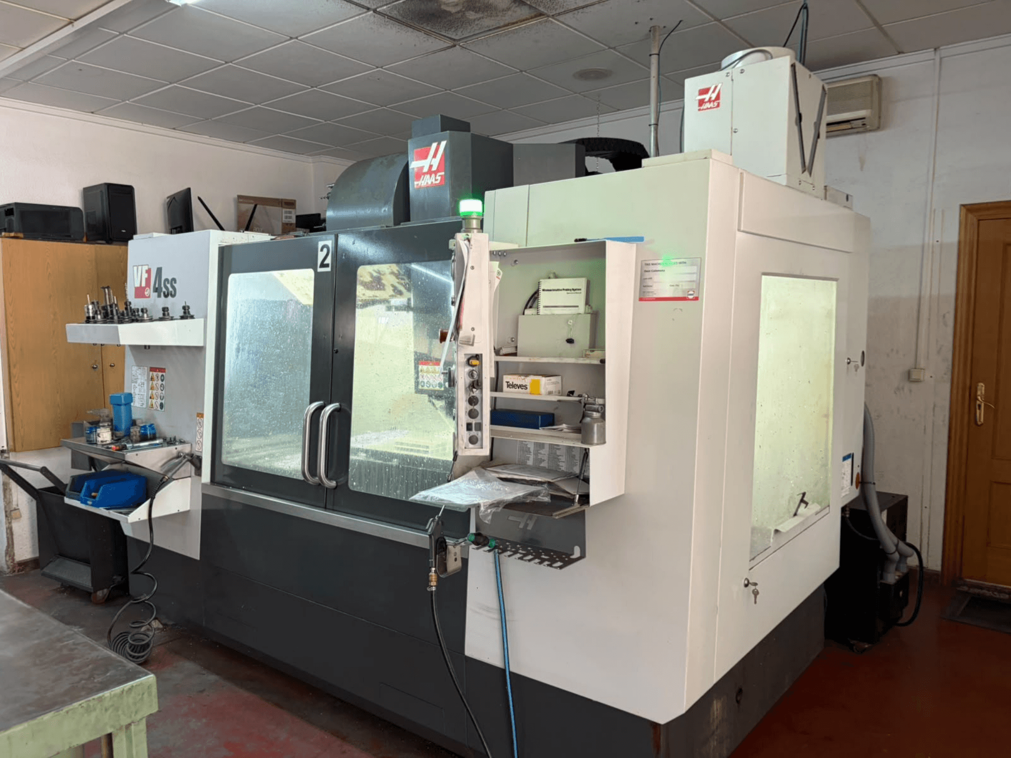 Centro de mecanizado vertical HAAS VF 4SS en un taller, vista frontal, en la que se aprecian el panel de control y la zona de trabajo con herramientas y materiales.