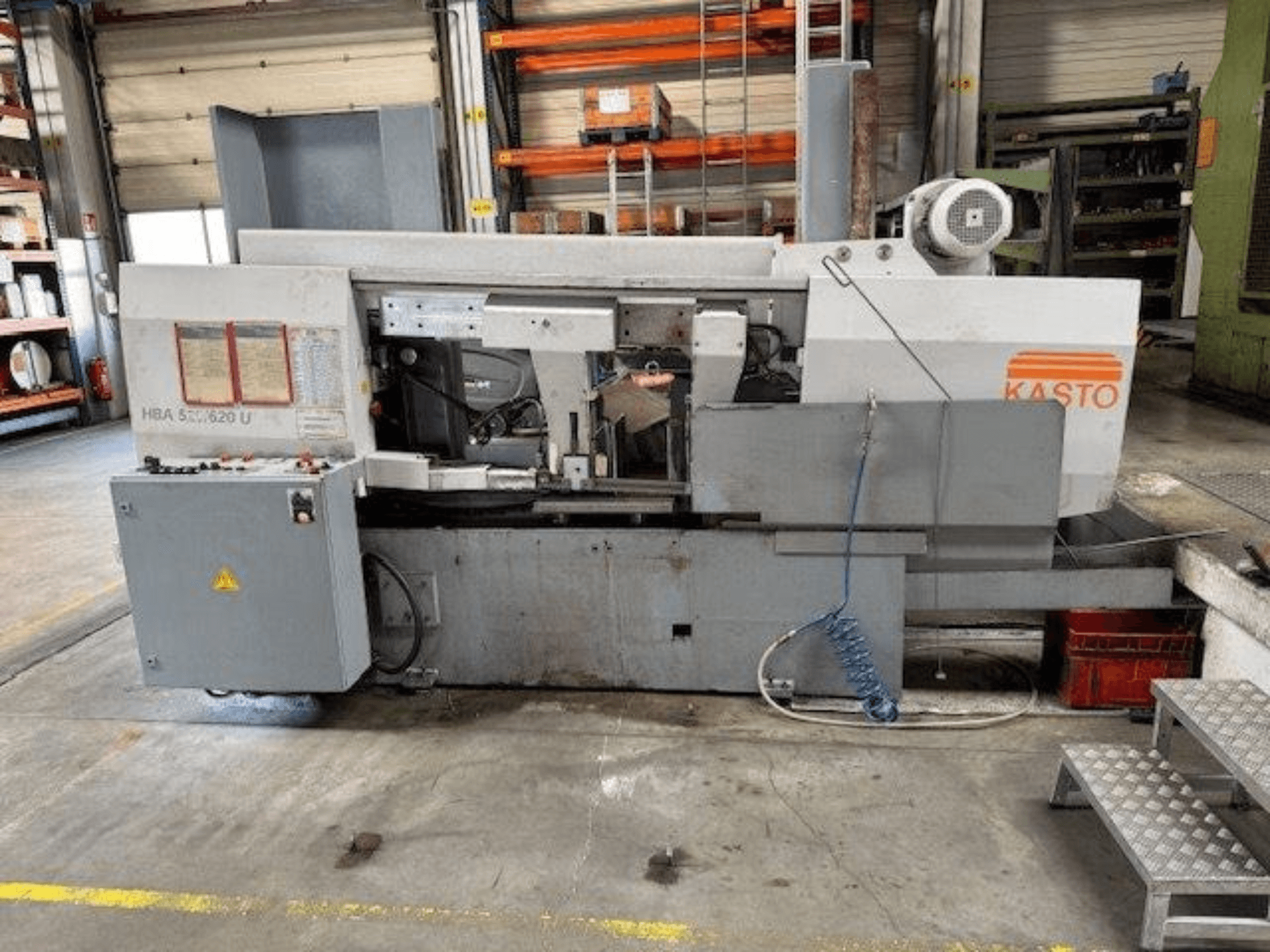 Sierra de cinta para metal KASTO HBA 520/620 U, vista lateral, mostrando el panel de control y la zona de corte en un taller.