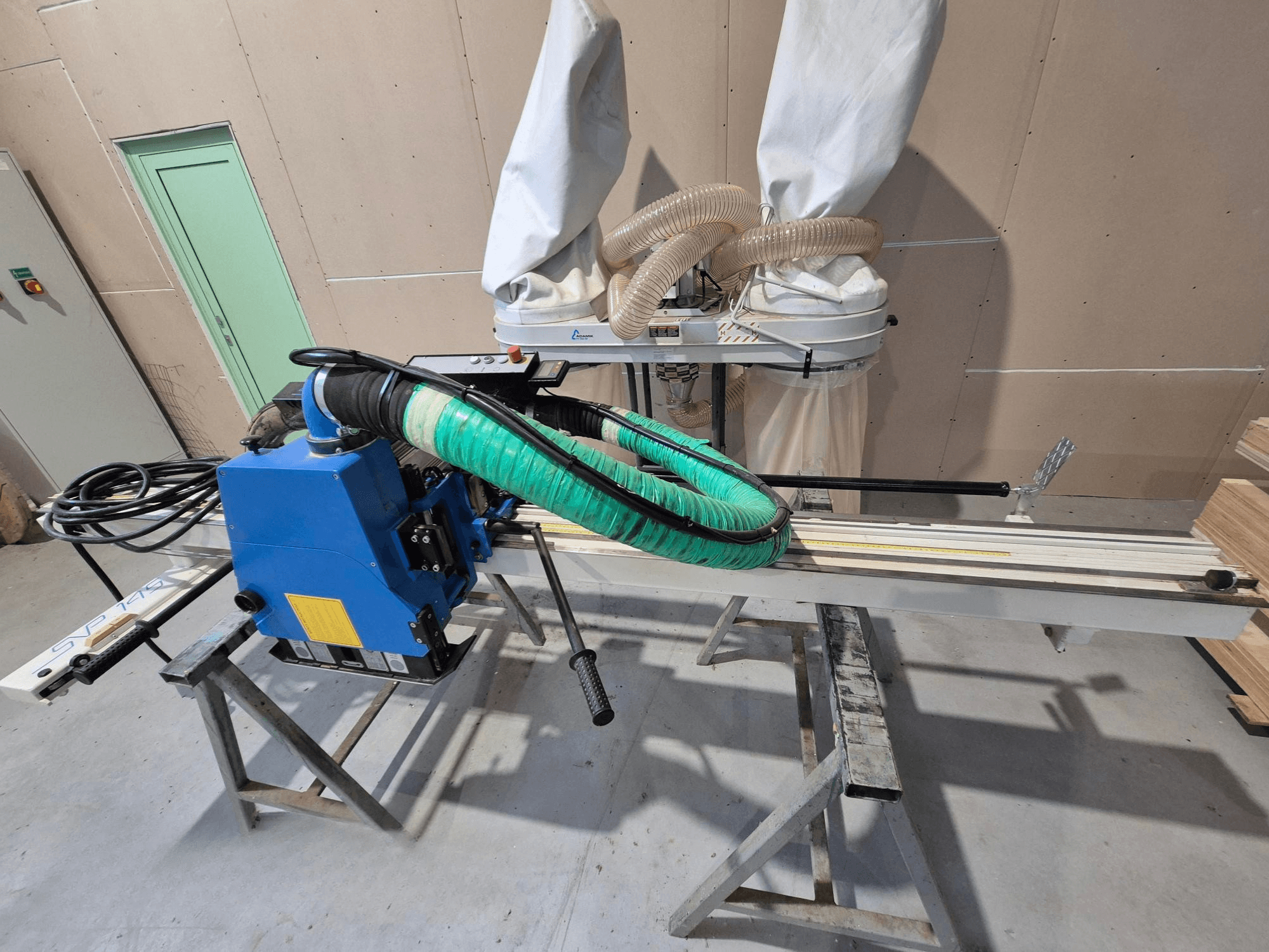 Sierra horizontal para tableros SVP-175 azul con manguera de polvo verde y soporte, vista de lado en un taller.