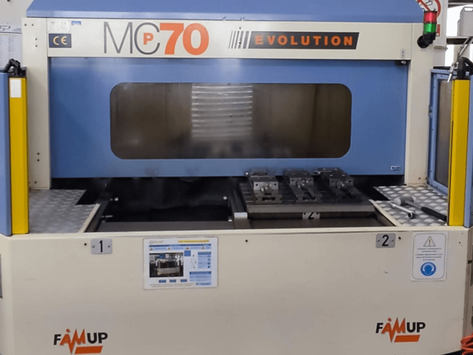 Centro de mecanizado vertical FAMUP MCP70 E, vista frontal mostrando el panel de control y el área de trabajo con útiles y elementos de seguridad.
