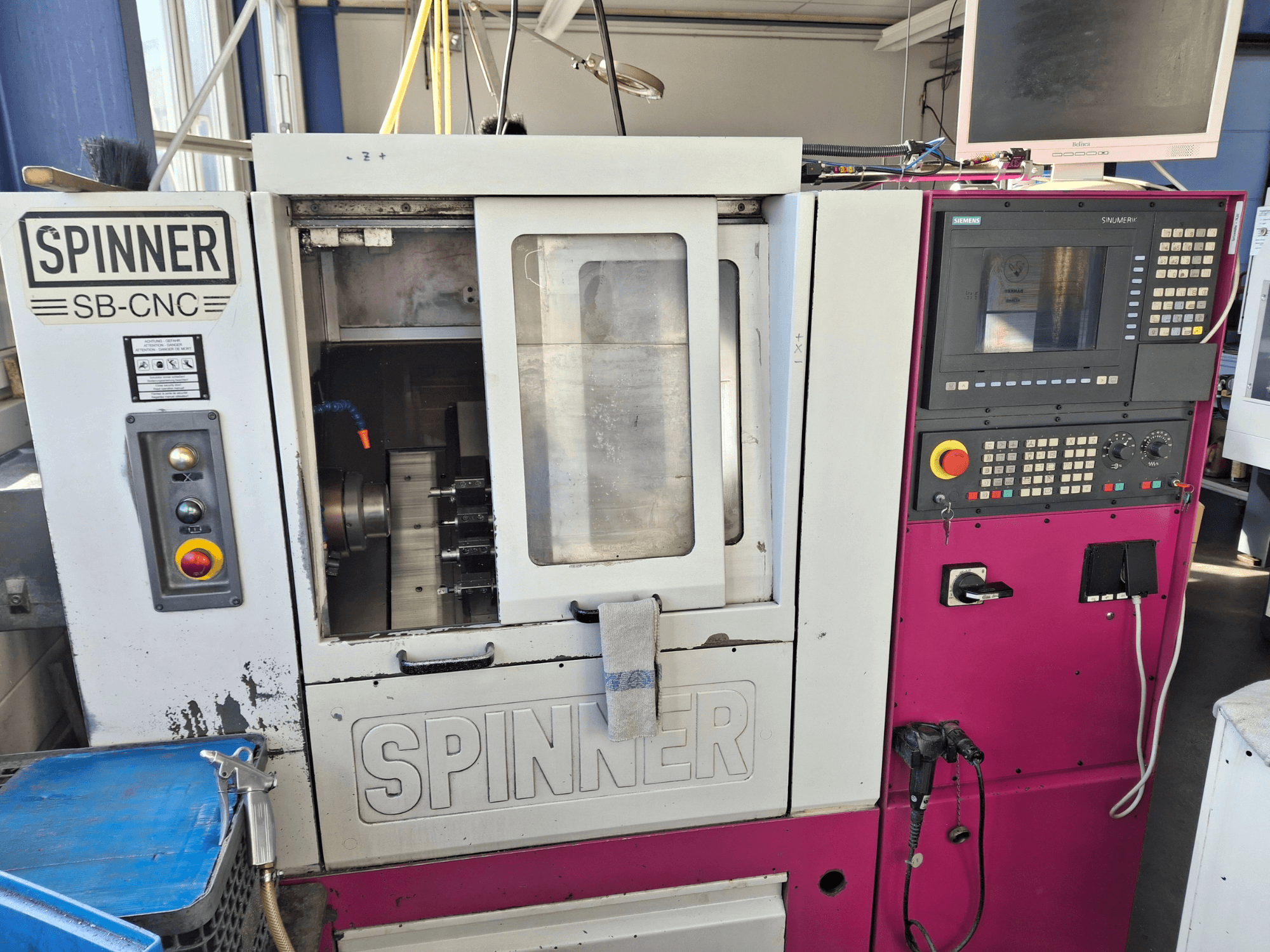 Máquina de torneado horizontal SPINNER SB-CNC, vista frontal que muestra el panel de control, el portaherramientas y los indicadores de funcionamiento.