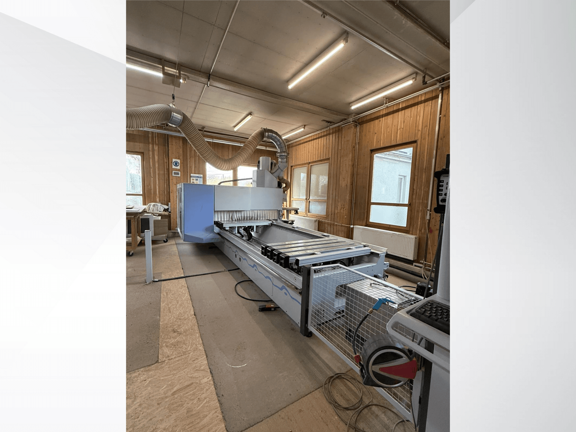 Fresadora CNC en un taller, vista lateral, con un gran cuerpo azul, cinta transportadora acoplada y panel de control visible.