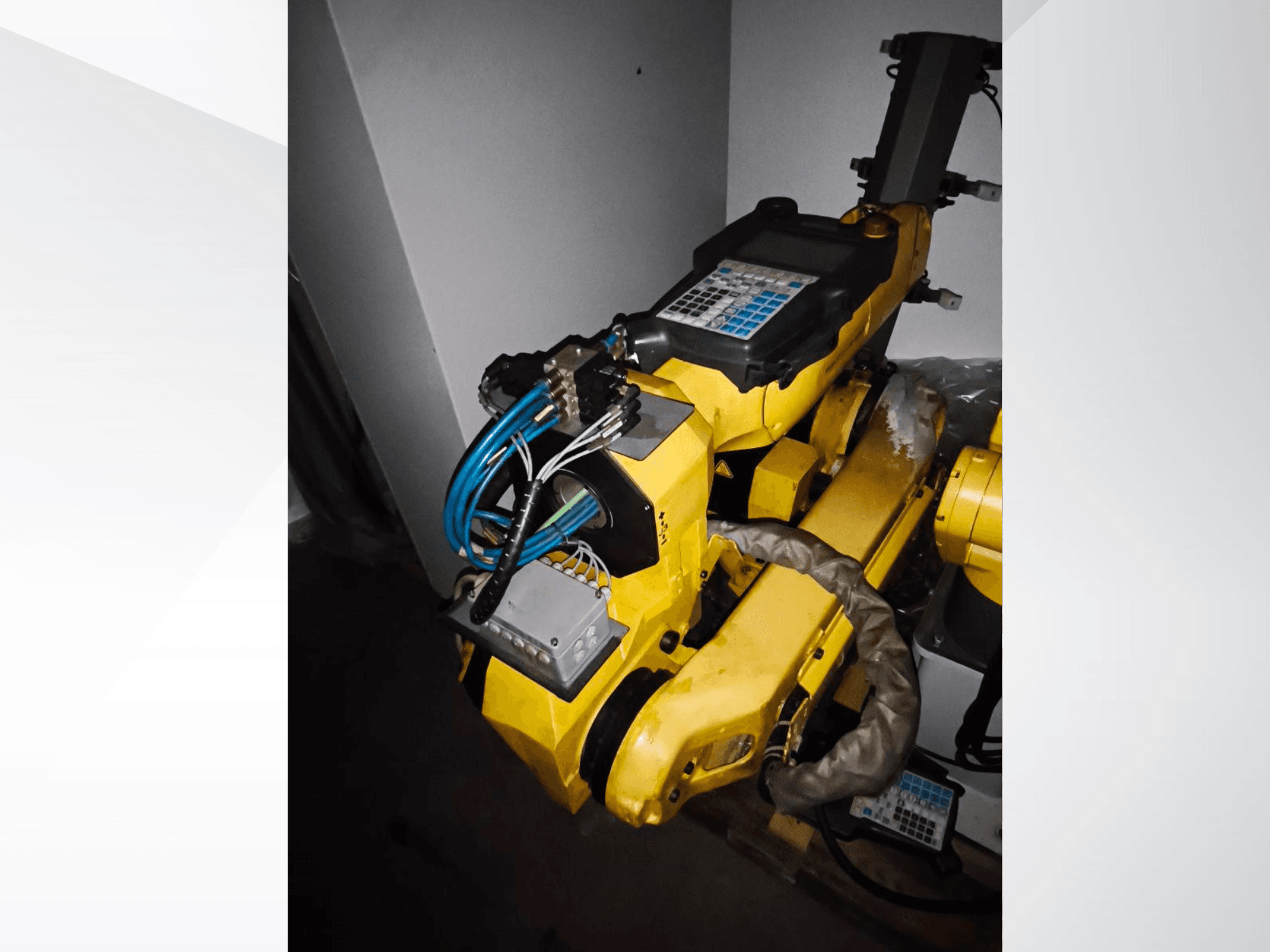 Brazo robótico FANUC M-20iA en una vista lateral, mostrando el cuerpo amarillo, el panel de control y el cableado conectado.