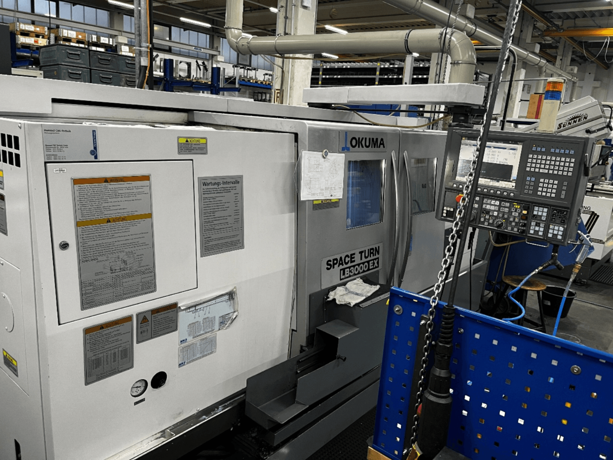 Máquina de torneado horizontal Okuma LB3000 EX, vista frontal, mostrando el panel de control y la información de seguridad en el lateral.