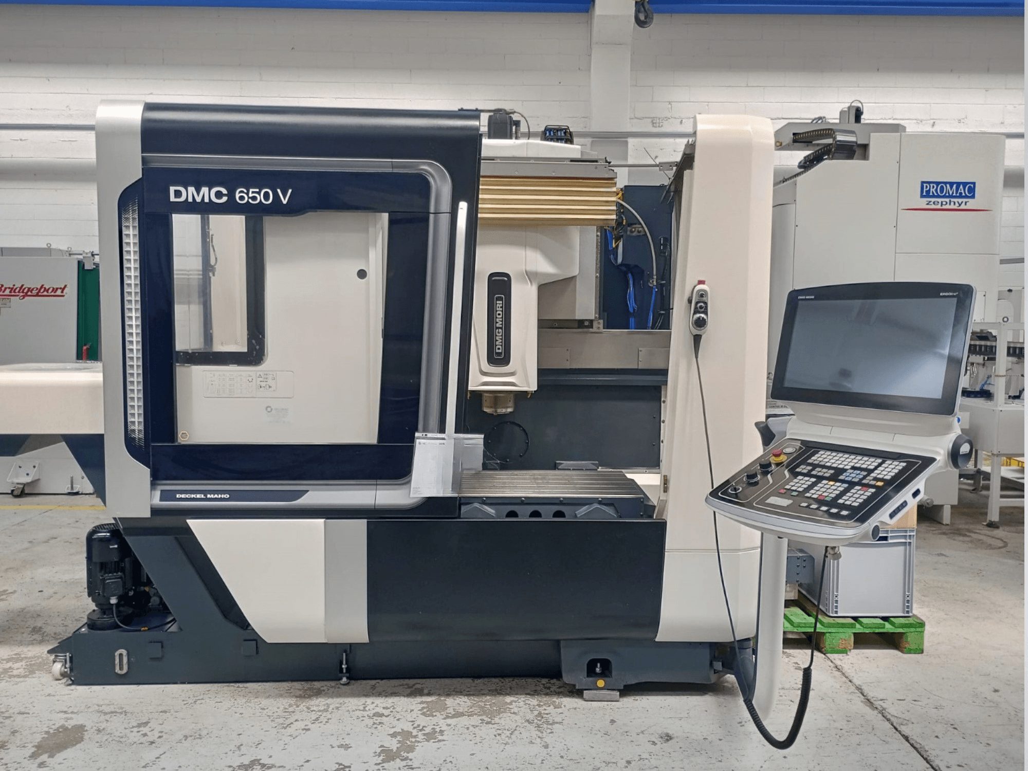 Vista lateral de la máquina CNC Decker Maho DMC 650 V, con un panel de control con botones y una pantalla, en un entorno industrial.