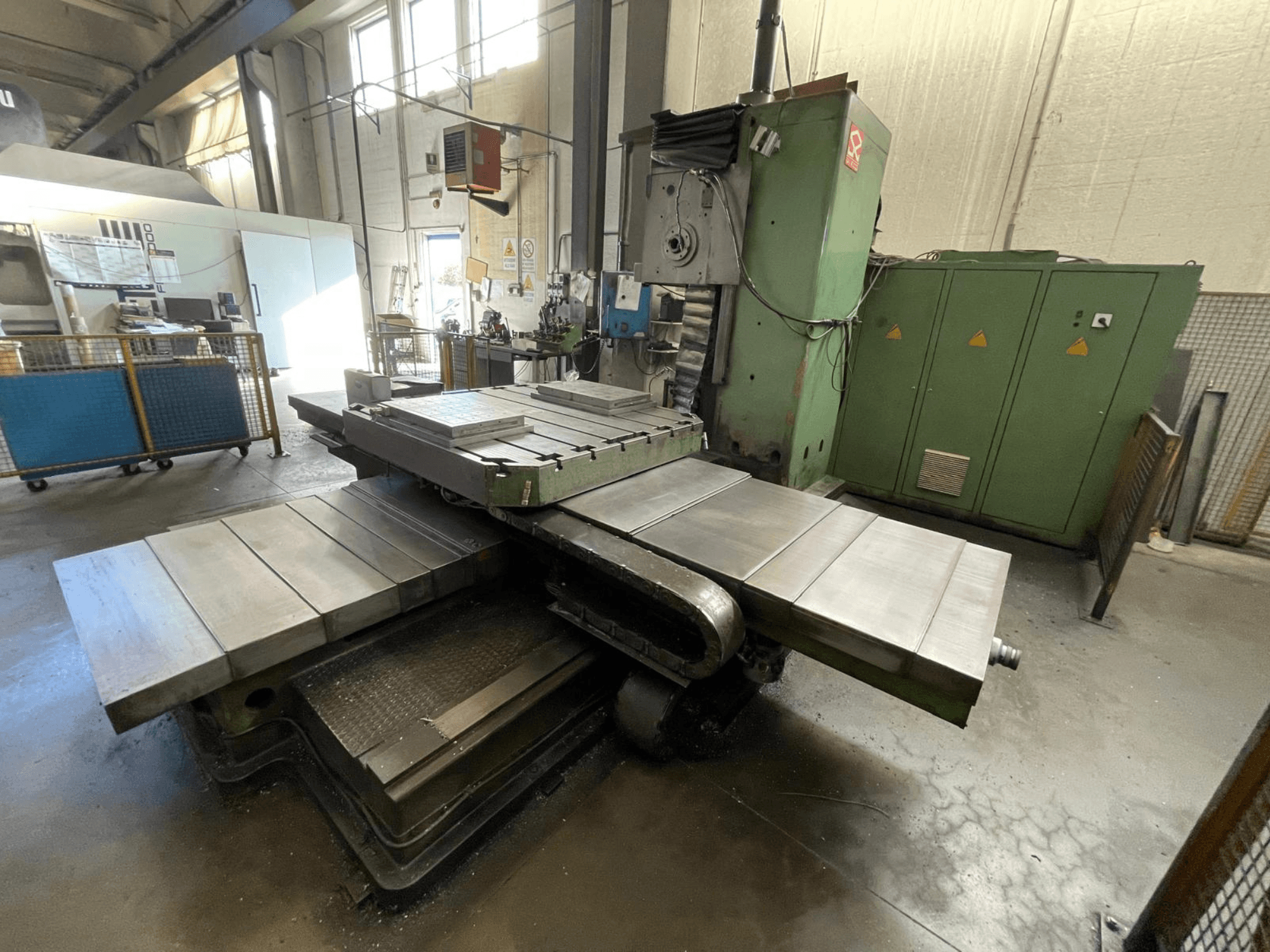 Fresadora industrial de gran tamaño con carrocería verde, vista lateral, con múltiples superficies planas y armarios de almacenamiento al fondo.