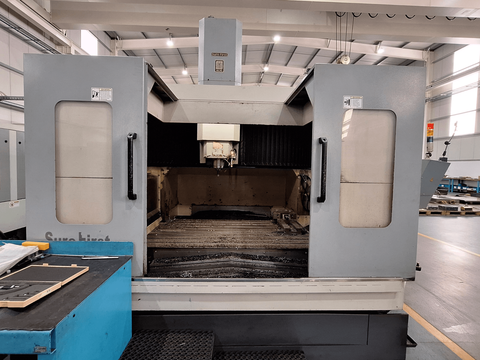 Centro de mecanizado vertical Sure First QM-1836, vista frontal mostrando el cabezal de herramientas y el área de trabajo vacía, entorno industrial moderno.