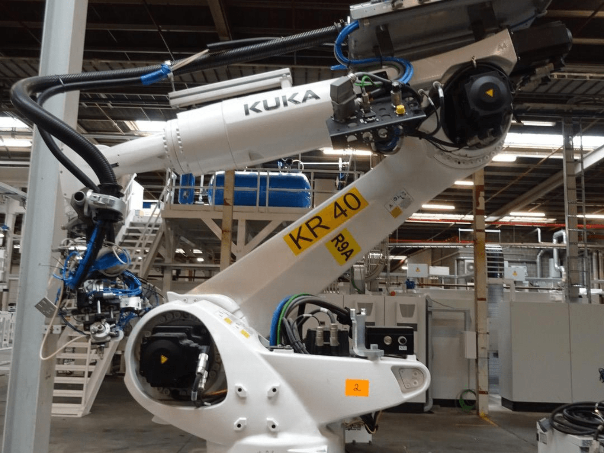 Brazo robótico KUKA KR 120 R3100-2 en vista lateral, mostrando el panel de control y los componentes mecánicos, situado en un entorno industrial.