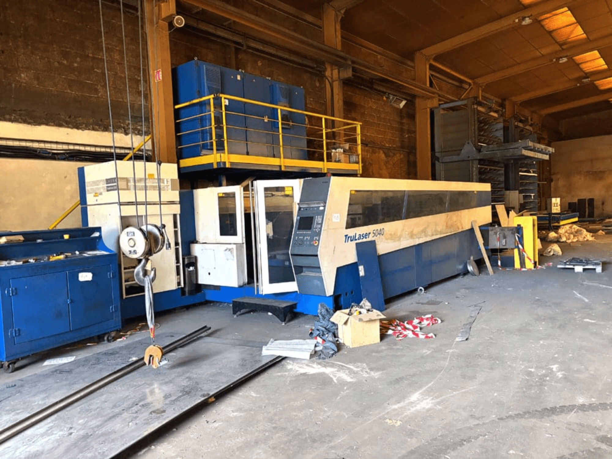Máquina de corte por láser de CO₂ de TRUMPF, modelo TRULASER 5040, fotografiada en un taller, vista frontal en ángulo con un fondo desordenado.