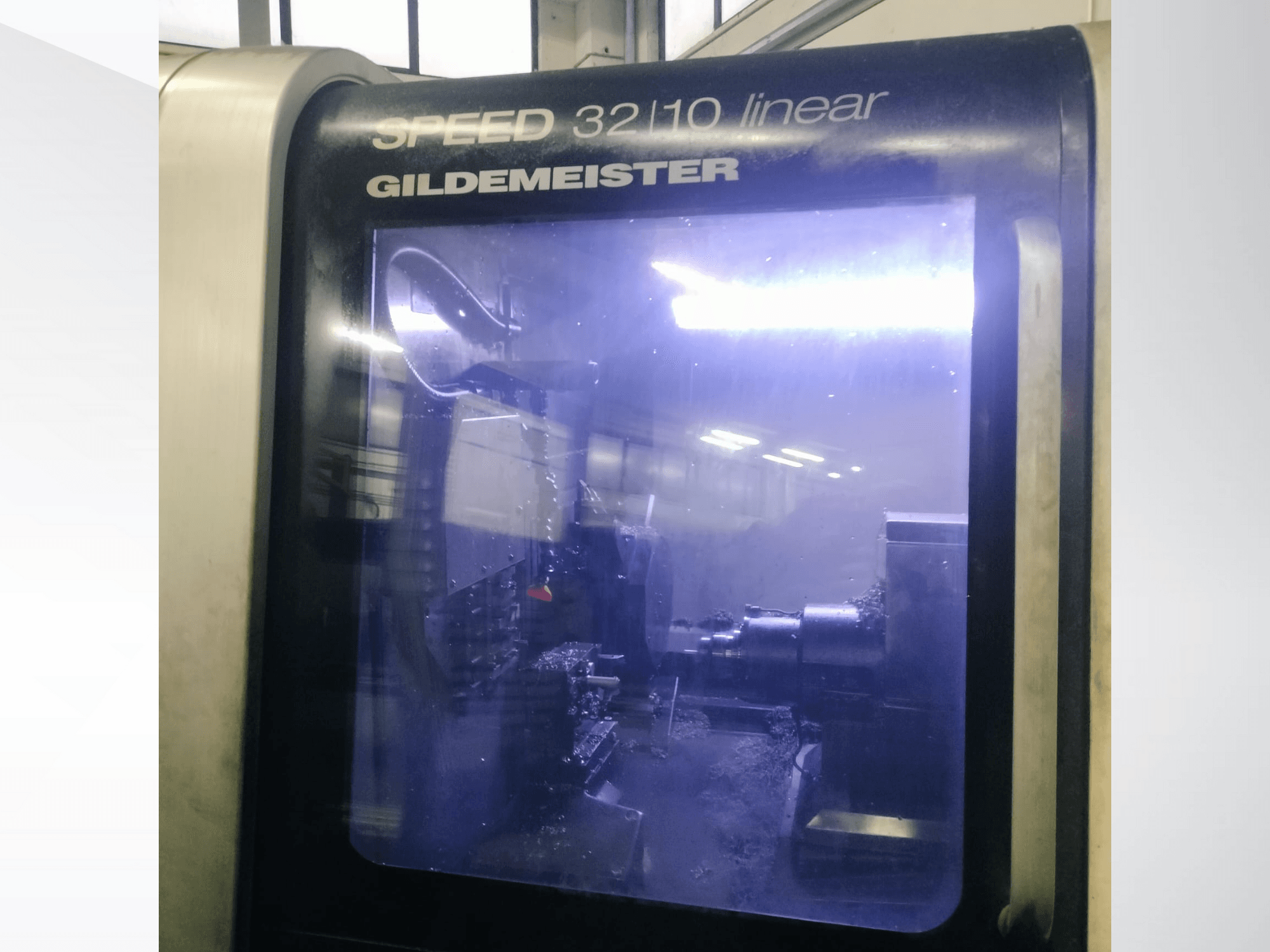 Vista frontal de la máquina CNC lineal SPEED 3210 de Gildemeister, mostrando los componentes internos y el refrigerante líquido en funcionamiento.