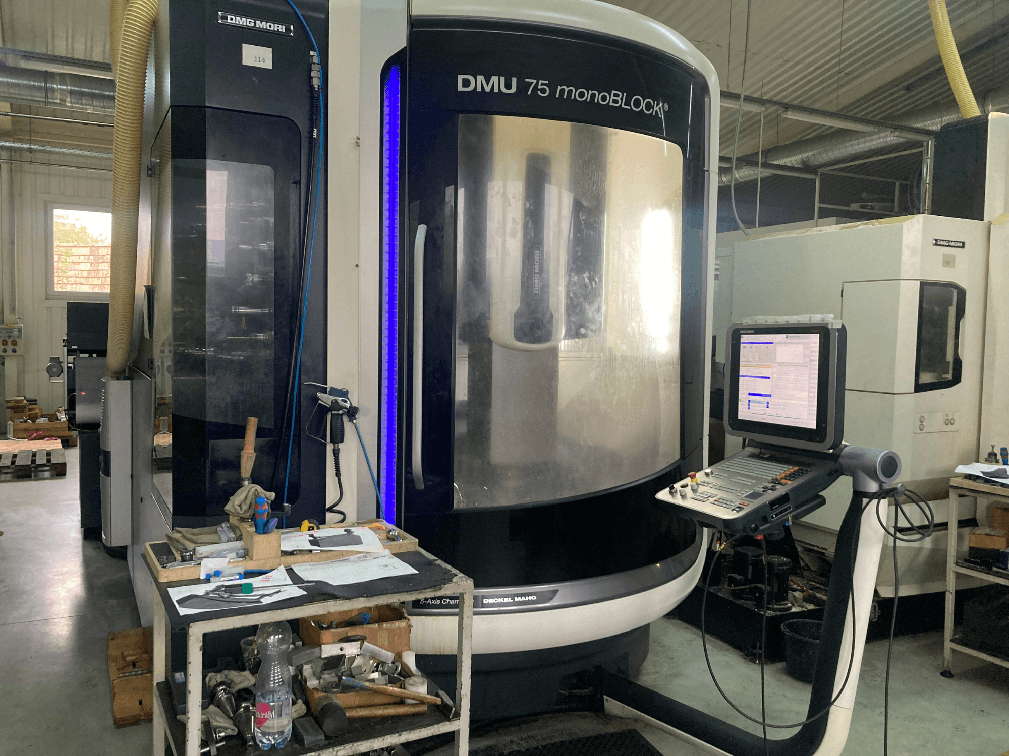 Máquina CNC DMG MORI DMU 75 monoBLOCK®, vista frontal, con panel de control, herramientas y un espacio de trabajo con materiales.