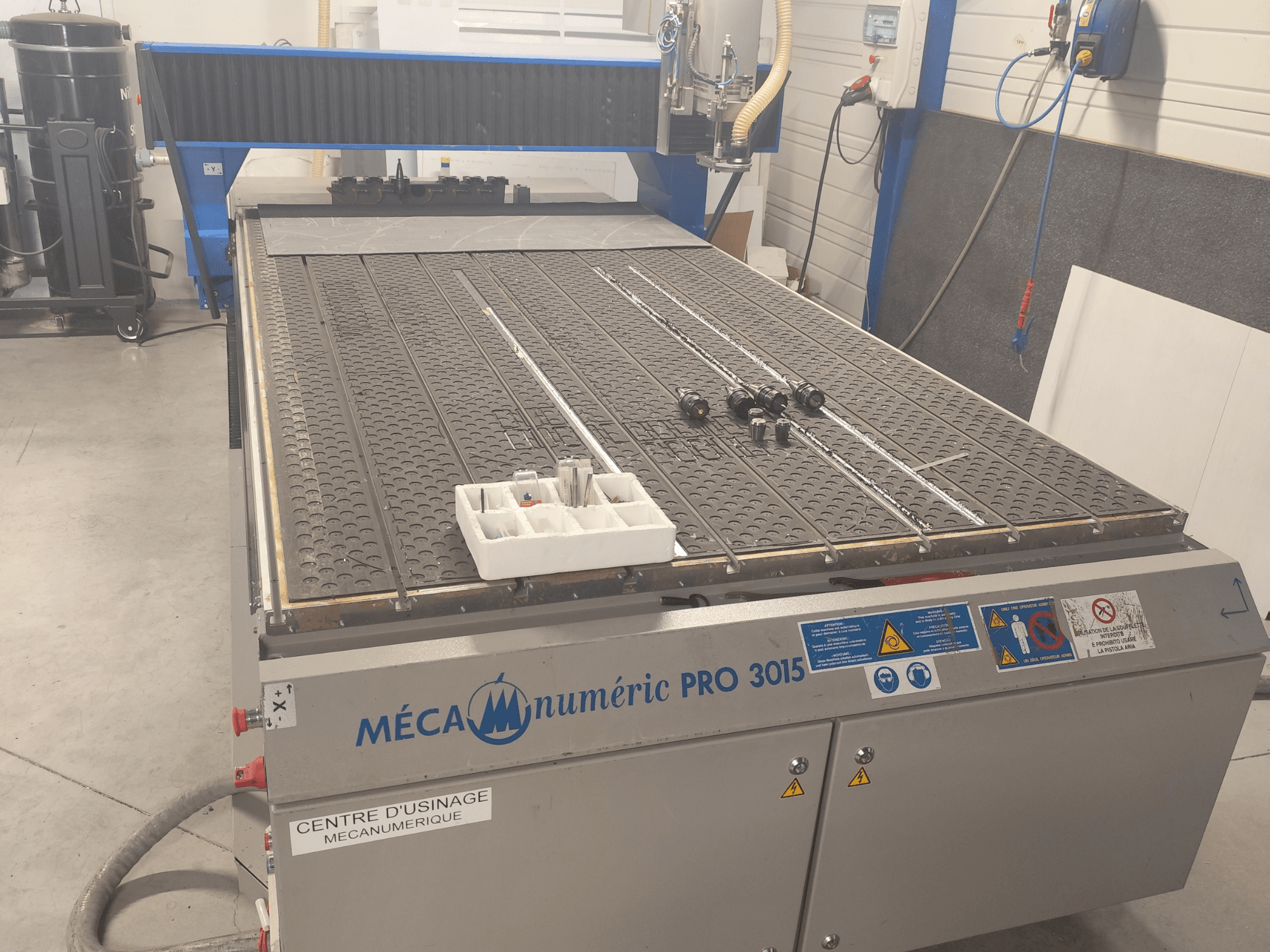 Vista frontal de la fresadora CNC MECANUMERIC Pro 3015, en la que se aprecian con detalle la mesa de corte, el panel de control y los accesorios colocados sobre la mesa.