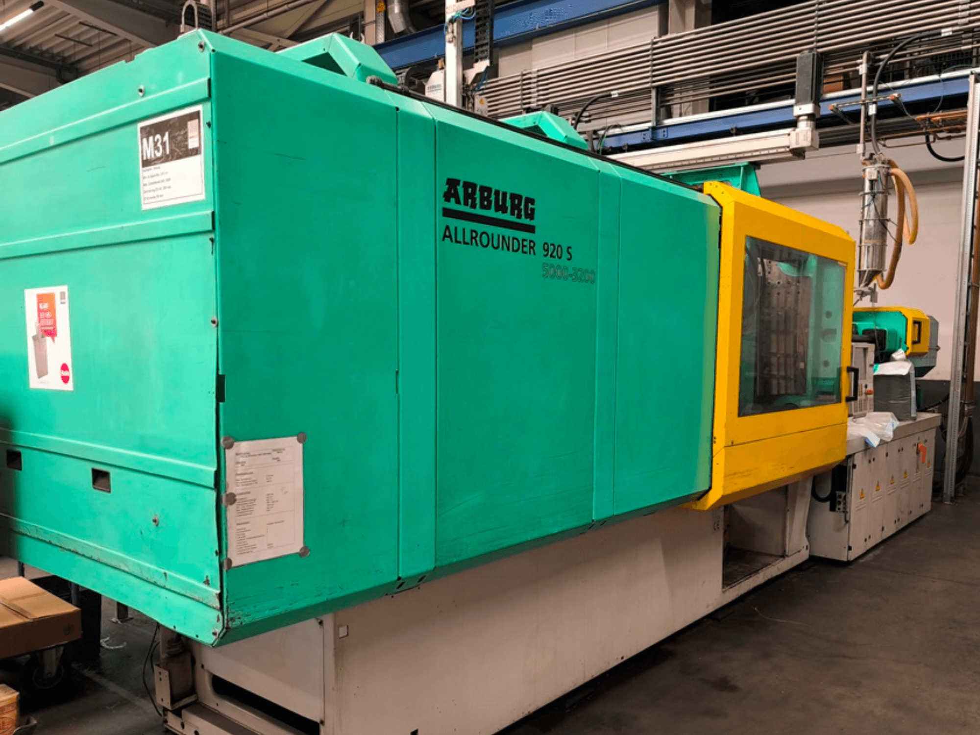 Máquina de moldeo por inyección Arburg Allrounder 920 S en azul agua y amarillo, vista lateral mostrando el panel de control y los componentes.