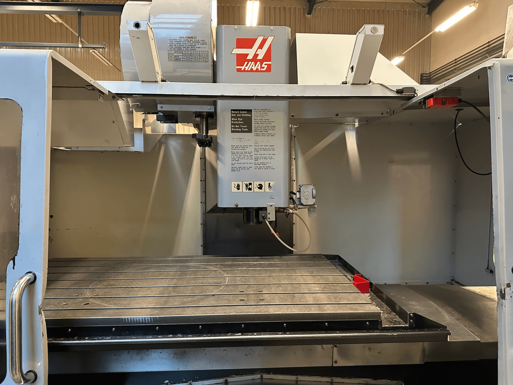 Fresadora CNC Haas, modelo VF-2, vista frontal que muestra los controles, la mesa de trabajo metálica y la etiqueta de seguridad en el panel.