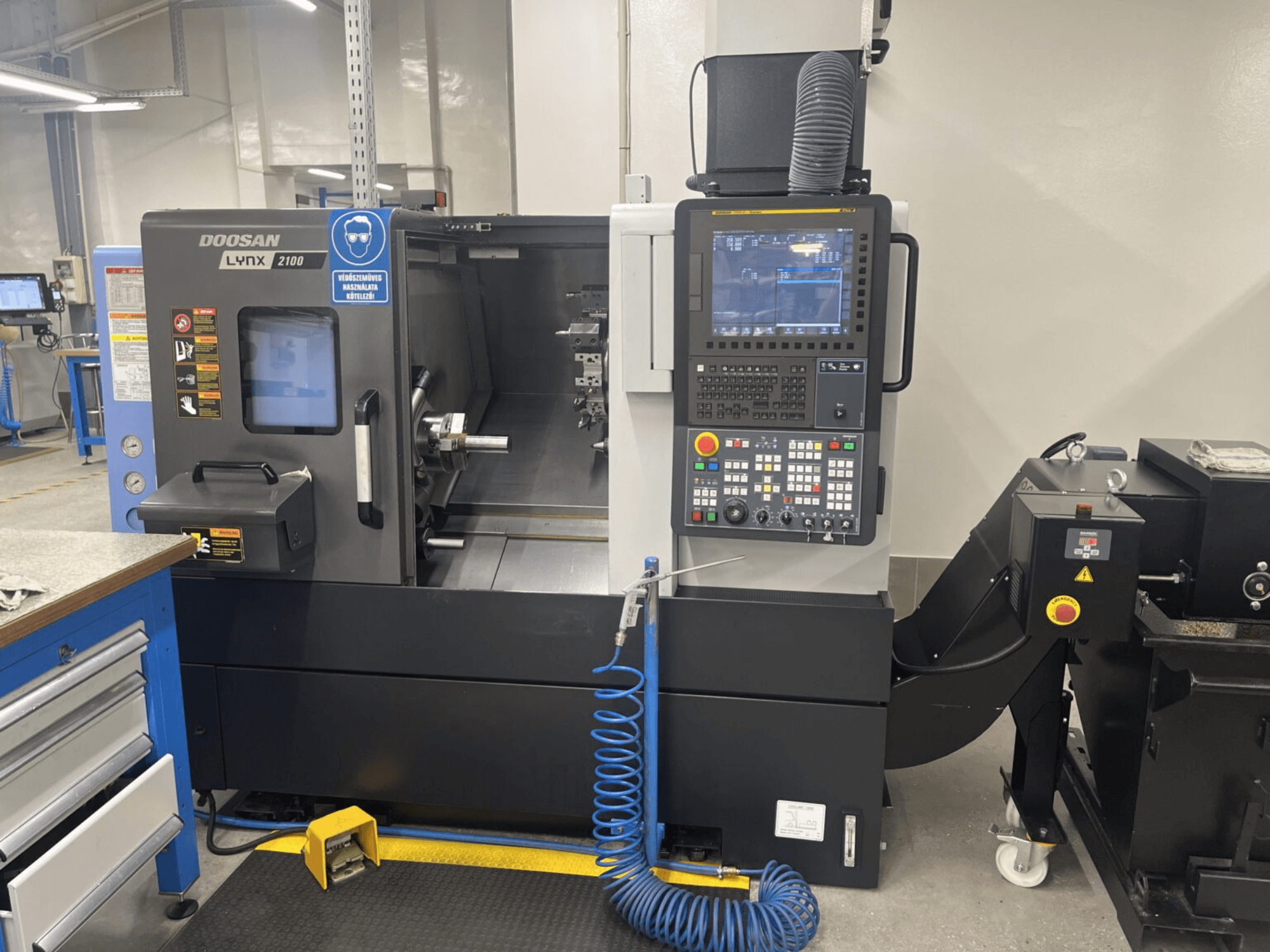 Vista frontal de un torno horizontal DOOSAN Lynx 2100A, que muestra el panel de control y la zona del husillo con notables características de seguridad.