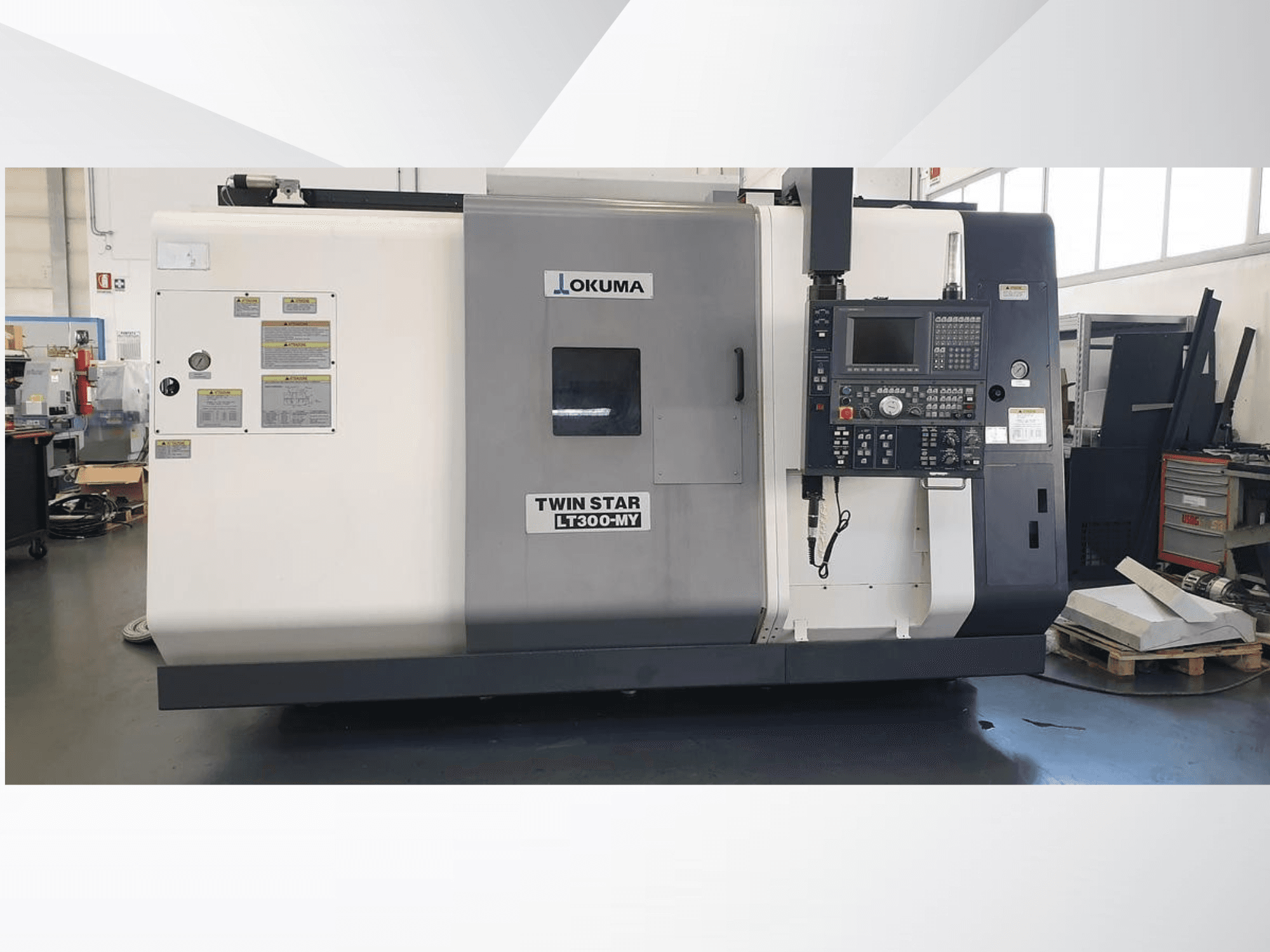 Máquina de torno CNC Okuma Twin Star LT300-MY, vista frontal con panel de control y etiquetas operativas visibles.