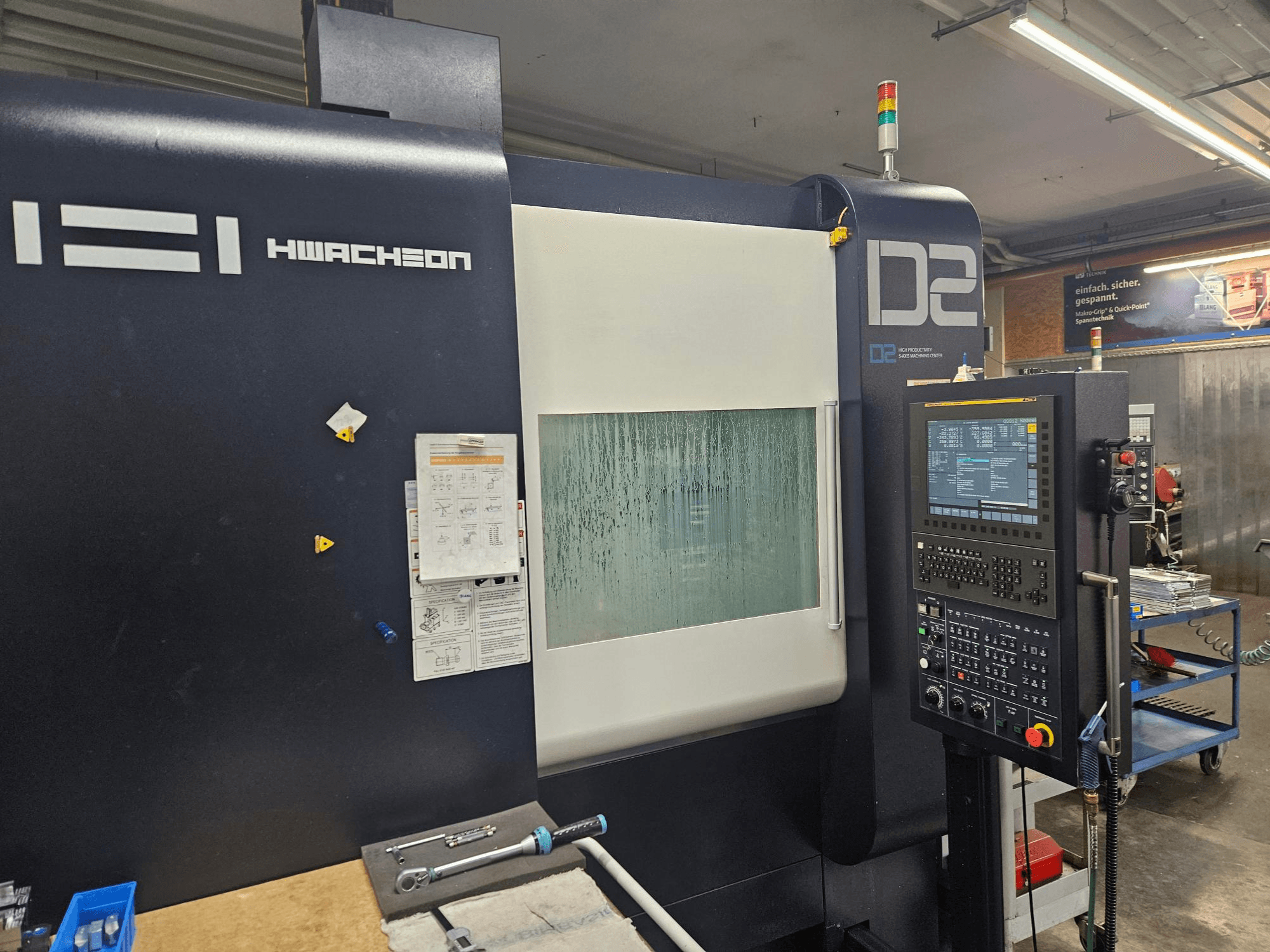 Centro de mecanizado vertical HWACHEON D2-5AX 12k, vista frontal en la que se aprecian el panel de control y la ventana de visualización empañada.