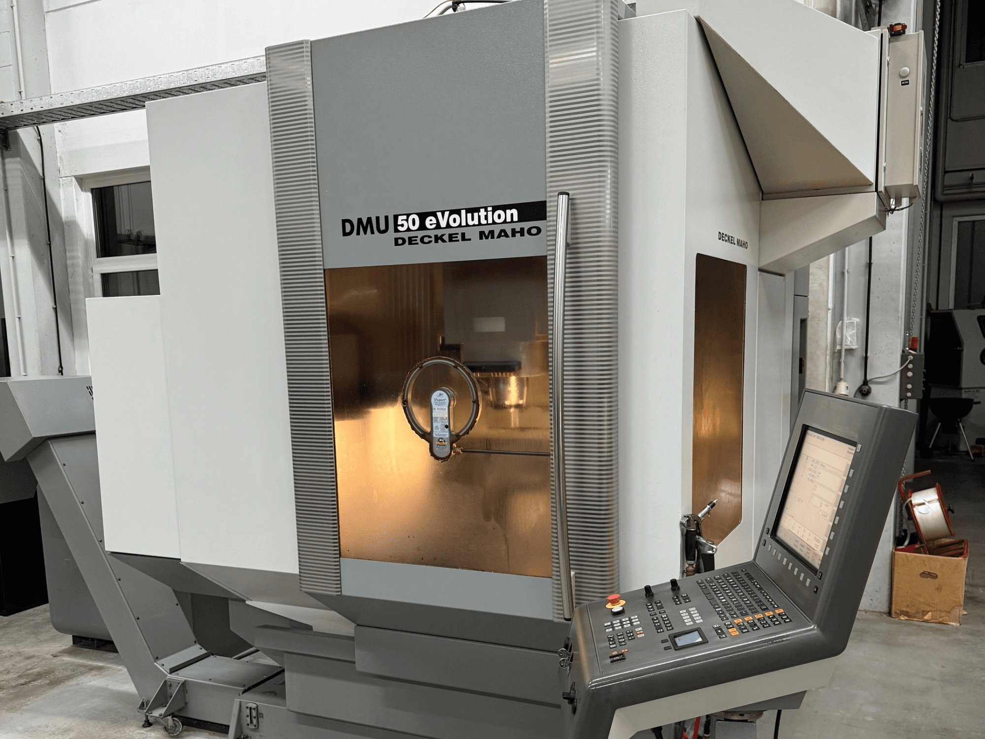 DMU 50 eVOLUTION de Deckel Maho, vista frontal de fresadora CNC con panel de control, superficie brillante y portaherramientas visibles.